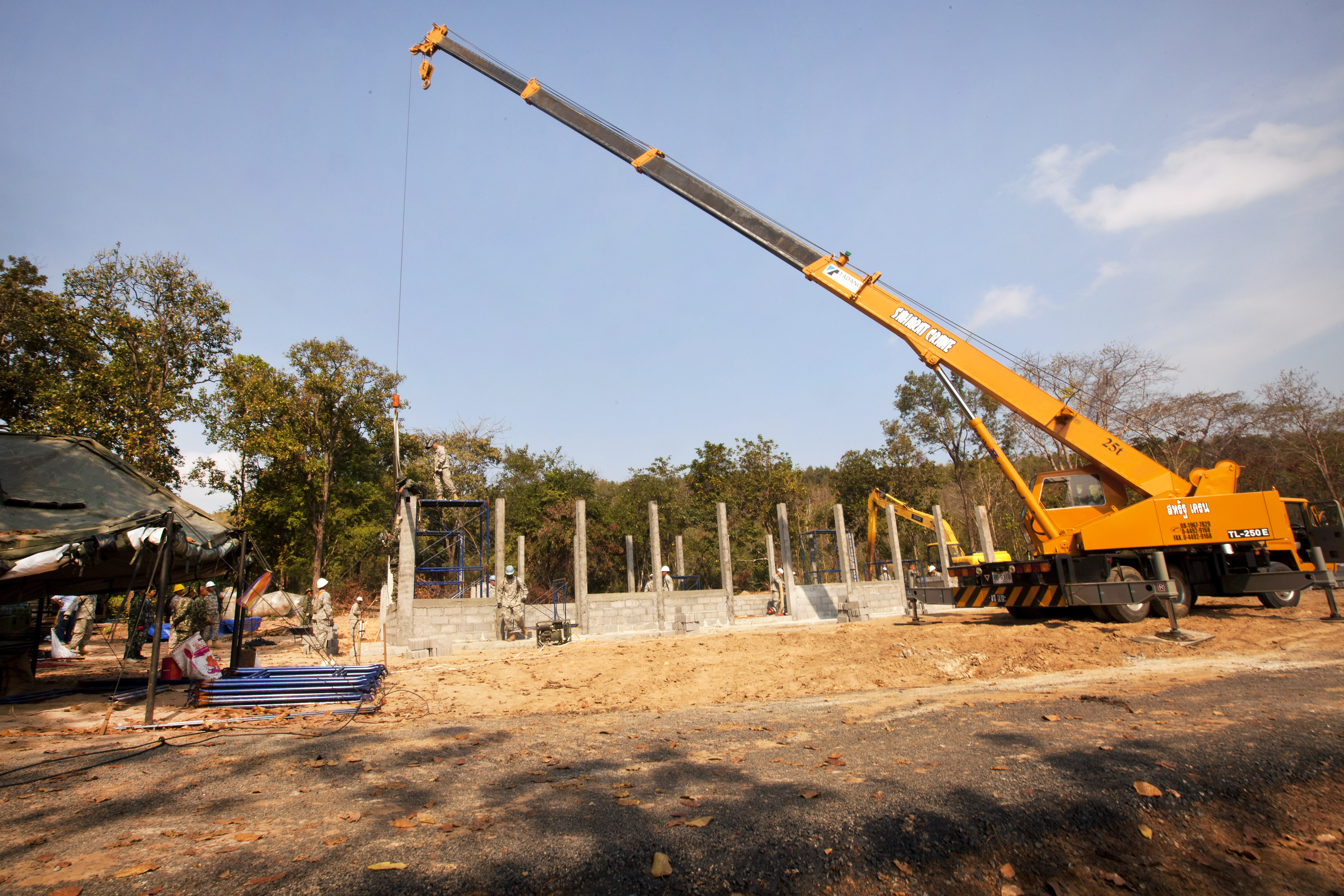 A Thai Soldier Operates A Crane To Lower A Metal Truss Onto A Multipurpose Building During
