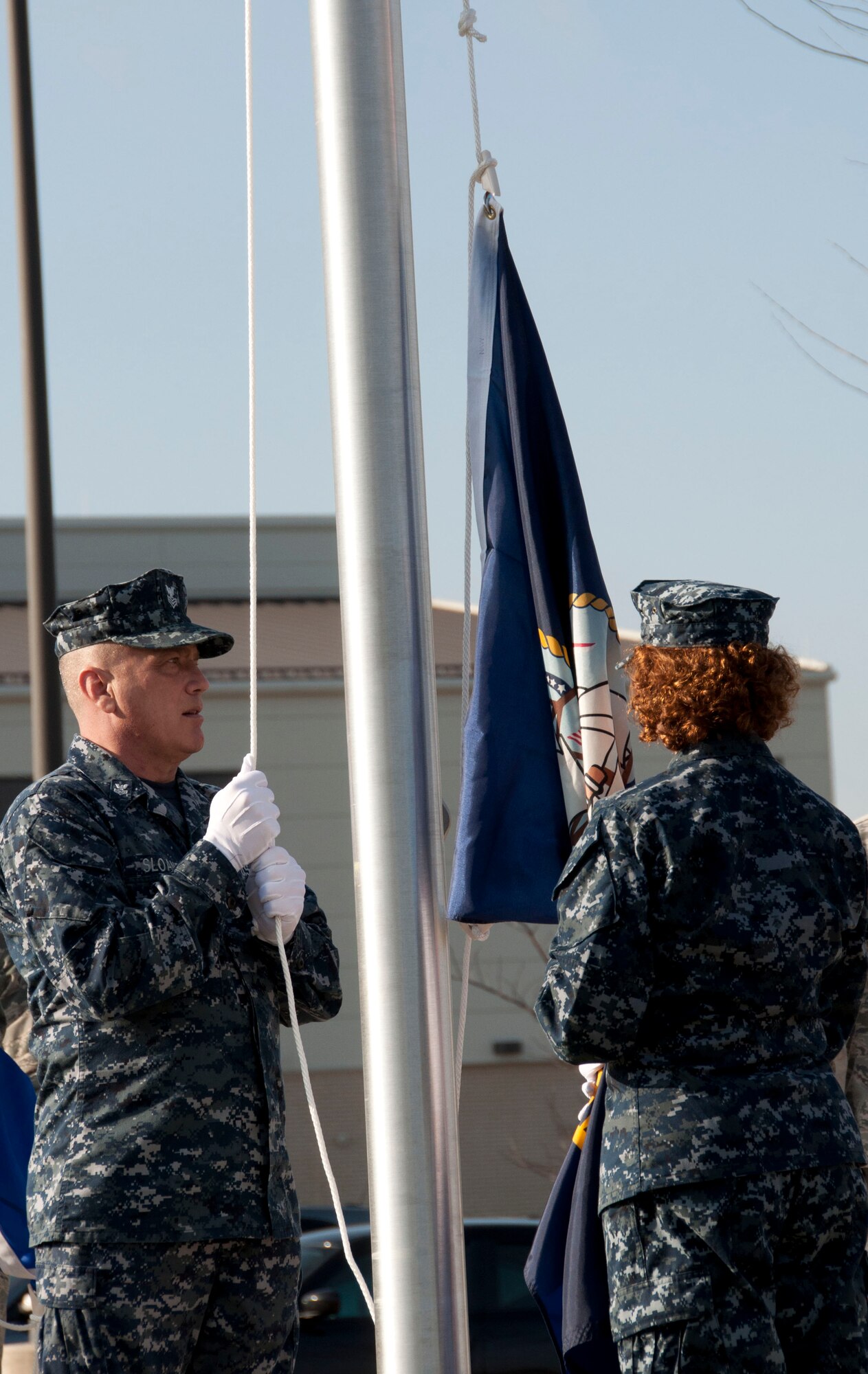 Petty Officer 1st Class Whit Sloane and Petty Officer 2nd Class Jennifer Howell raise the U.S. Navy Flag at the Memorial Flag Circle in front of the Charles C. Carson Center for Mortuary Affairs, Dover Air Force Base, Del., Jan. 24, 2012. Sloane is a Navy mortician assigned to Millington, Tenn., and Howell is a Navy mortician working with the liaison team at the mortuary here. (U.S. Air Force photo/Staff Sgt. James. W. Jackson)