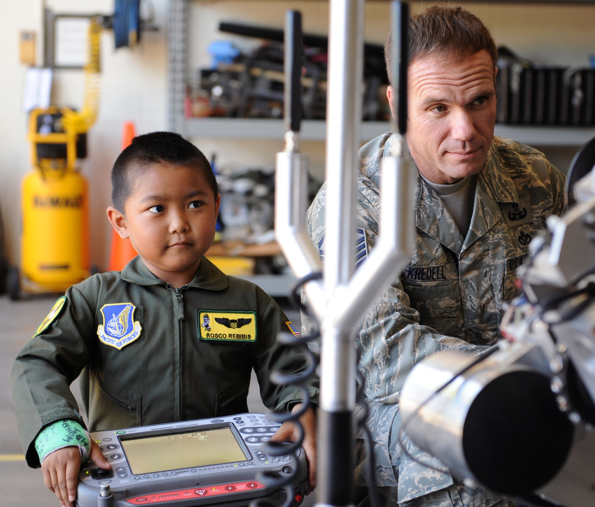 Rosco Rebibis, a patient at Kapiolani Medical battling acute lymphoblastic leukemia, operates a bomb robot with the help of Master Sgt. Matthew Kredell, 647th Civil Engineer Squadron explosive ordnance disposal flight chief, June 29 as part of the Pilot for a Day program at Joint Base Pearl Harbor-Hickam, Hawaii. ALL is a cancer of the blood and bone marrow and is the most common type of cancer in children. (U.S. Air Force photo by Staff Sgt. Nathan Allen)