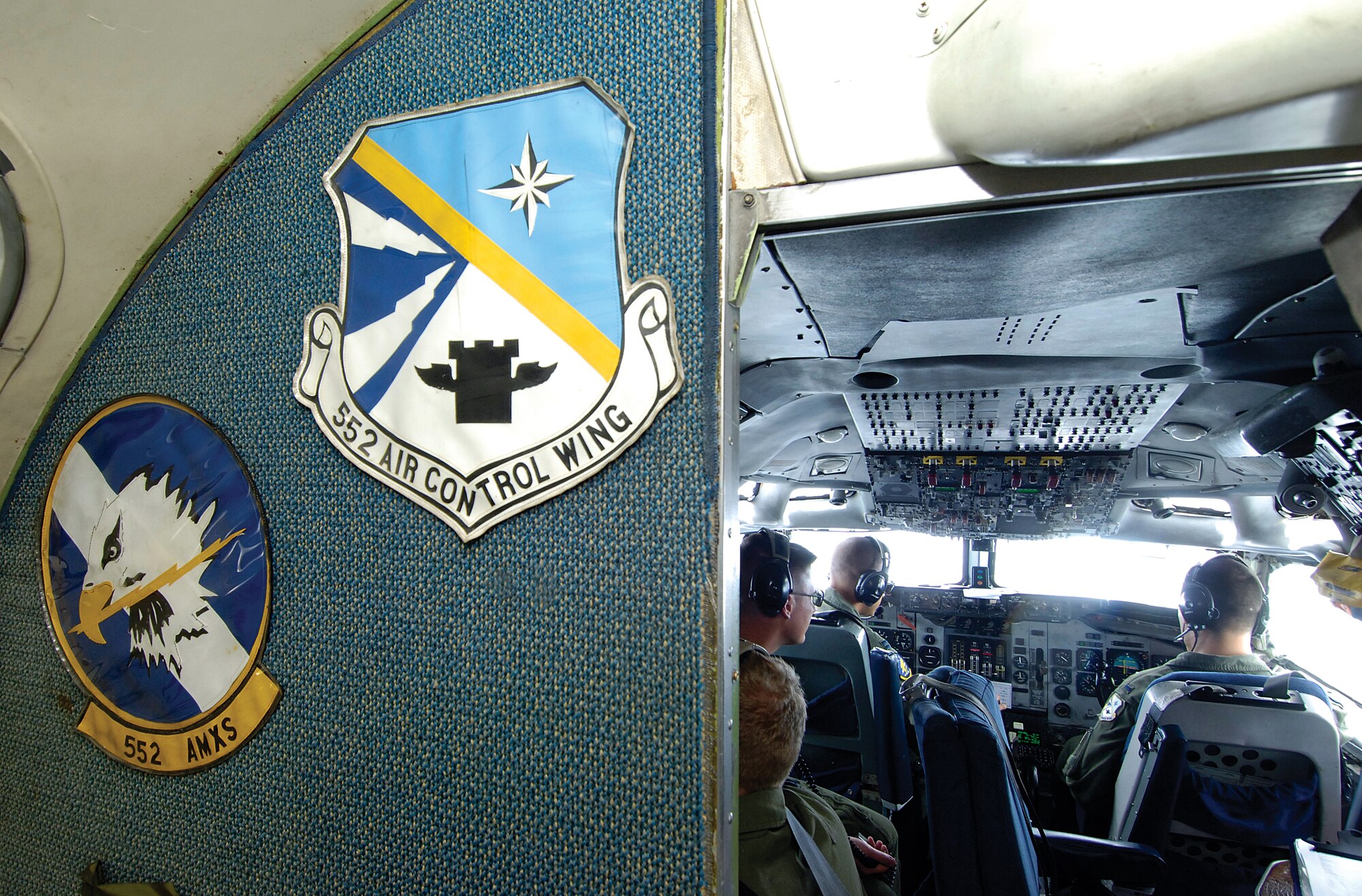 Oversized emblems attached to a wall of an E-3 Sentry jet lead to the cramped cockpit where five members navigate and fly the AWACS during a June 11 training mission. High over the bright clouds of a developing Missouri thunderstorm, the crew works through checklists and reacts to emergency training, keeping themselves ready for the real-world call. (Air Force photo by Margo Wright)