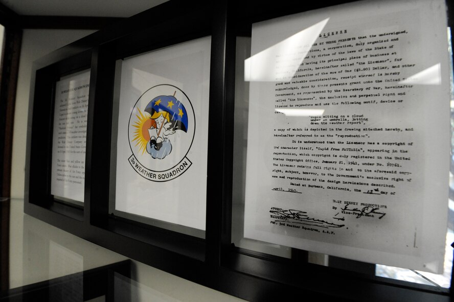 A frame containing the 3d Weather Squadron’s patch and signed contract showing the design, which was licensed from the Walt Disney Company to the government for $1, sits in the heritage room of the 3d WS, Fort Hood, Texas, June 25, 2012. The patch shows the character Cupid from the Disney movie “Fantasia” jotting down the weather forecast while sitting on a cloud between sun and rain. He is wearing a “Sherlock Holmes” hat symbolizing the unit’s mission of weather investigation and prediction.(U.S. Air Force photo by Staff Sgt. Joshua J. Garcia/Released)