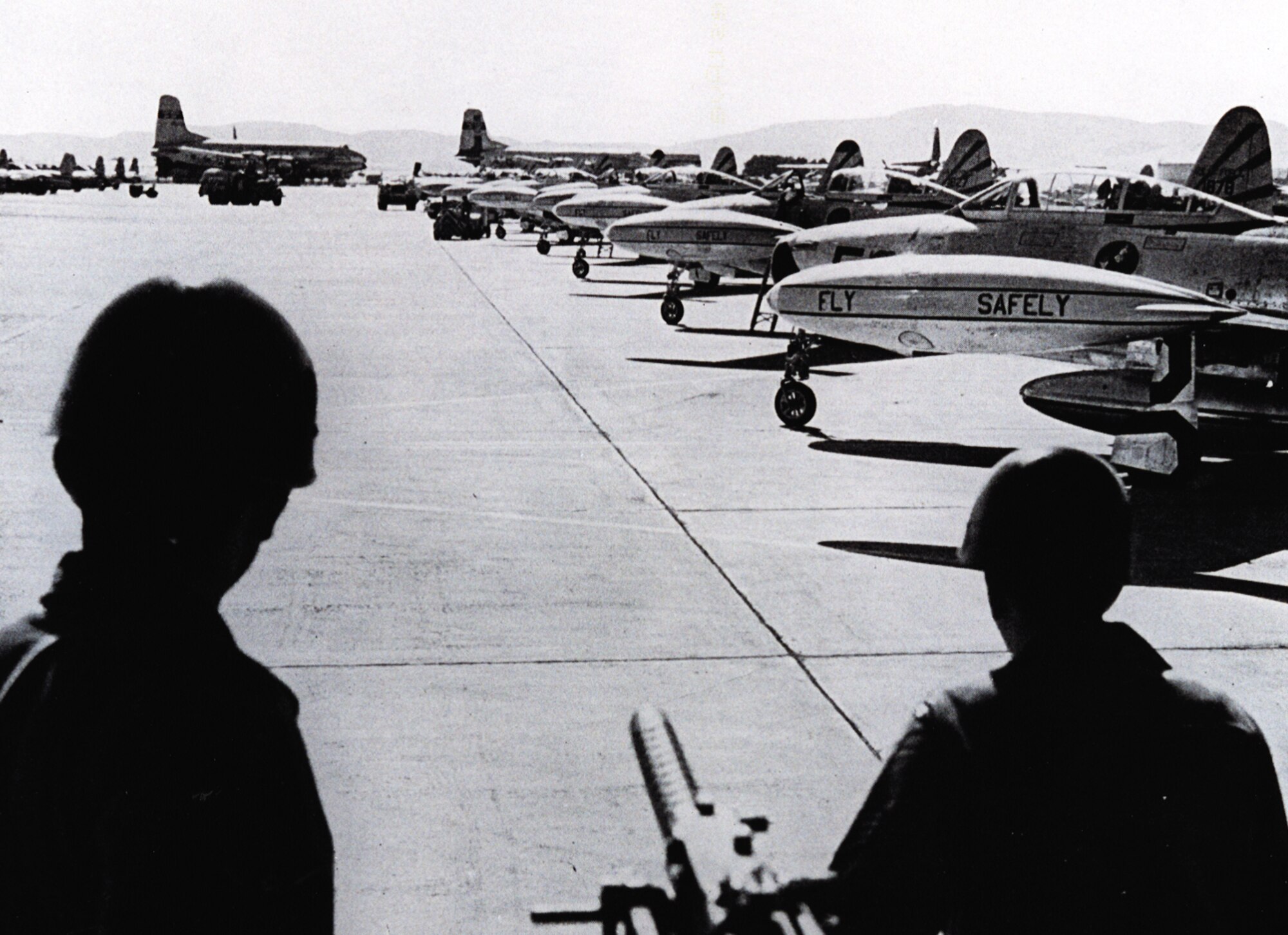 Two Air Policemen at Travis Air Force Base, Calif., monitor a flightline full of 31st Fighter Escort Wing F-84Gs prior to the fighters' launch for Hickam AFB, Territory of Hawaii, as part of Operation Fox Peter One. The large transport aircraft in the background are Military Air Transport Service C-74 Globemasters, part of the support force. (courtesy photo)