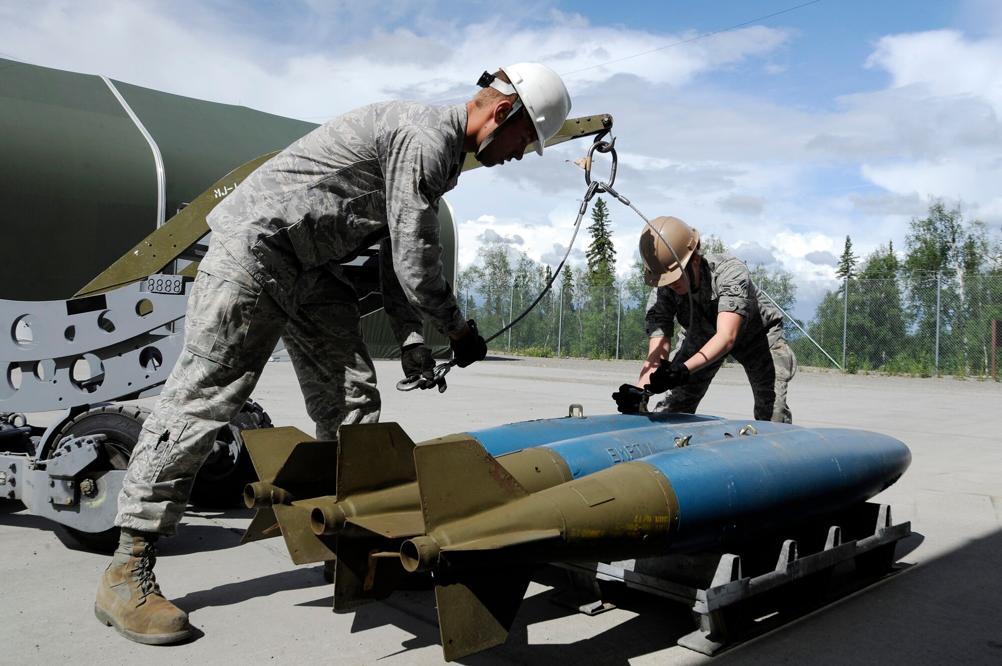 U.S. Air Force Airmen 1st Class John Berthold and Amberlyn Hawkins, 51st Munitions Squadron munitions crew chiefs, prepare to hoist bomb dummy units with a bomb lift July 2, 2012, Eielson Air Force Base, Alaska. Munitions crew chiefs specialize in assembling, storing and transporting munitions dropped by a wide range of aircraft. (U.S. Air Force photo/Staff Sgt. Jim Araos)