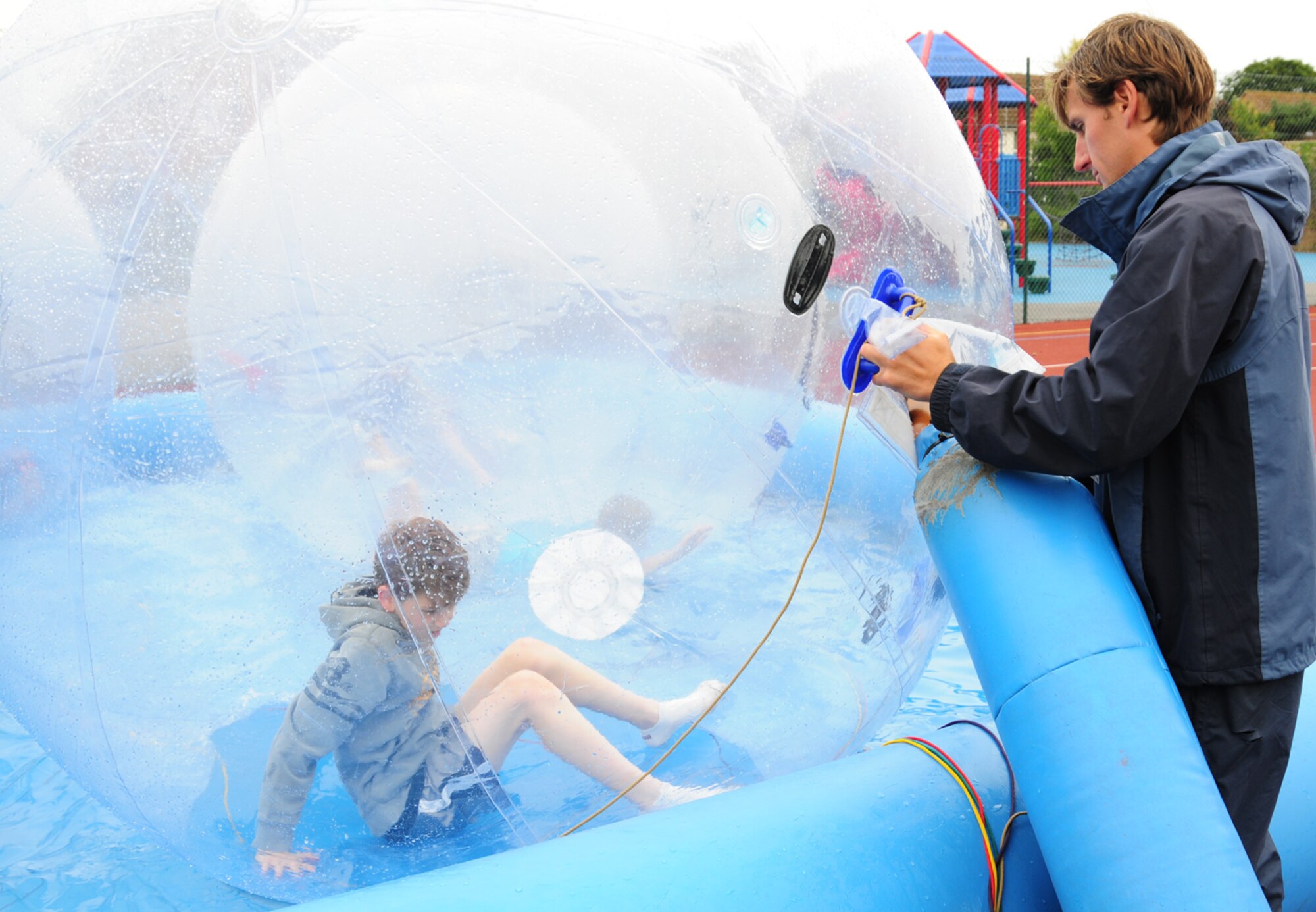 RAF MILDENHALL, England – William Gray, right, helps Shaun Freeman, 12, into a zorb before sealing up the entry and exit hole July 2, 2012. Children from the youth center at RAF Mildenhall had the chance to try water zorbing, which is just one of many activities available for children at the youth center during the school holidays. (U.S. Air Force photo/Karen Abeyasekere)