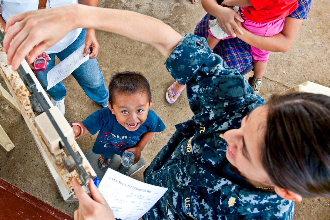 U.S. Navy Ensign Alex Tonsberg weighs a Filipino child at a medical project site during Pacific Partnership 2012 at the Carayman Elementary School in Samar province, Philippines, June 28, 2012.
