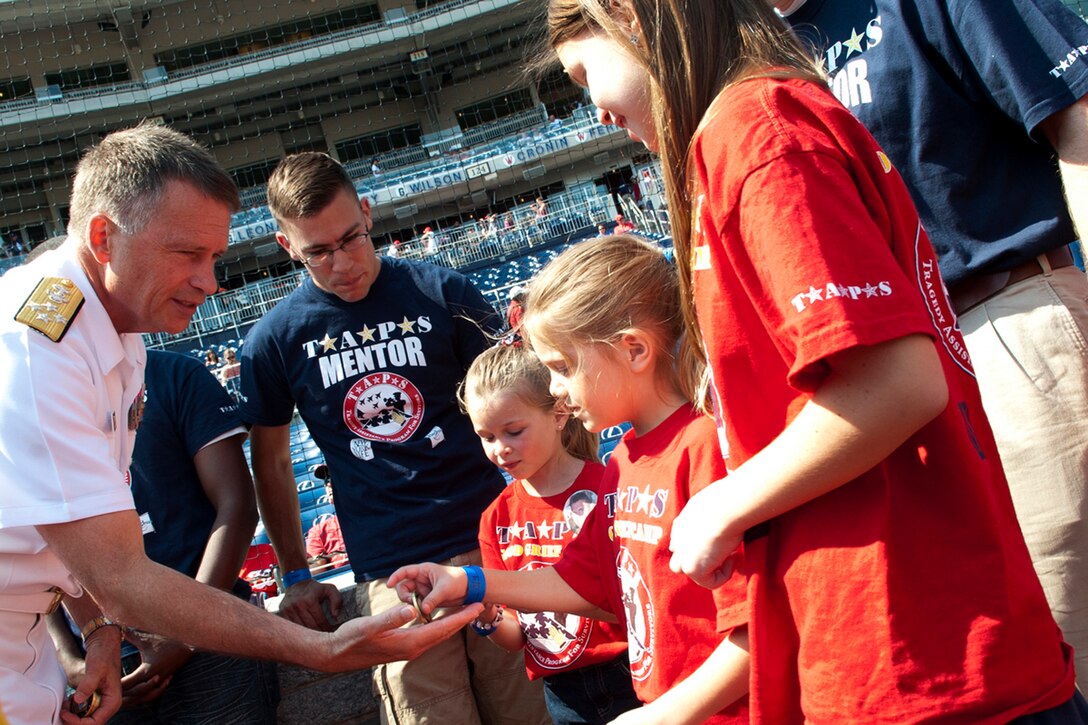 Navy Adm. James A. Winnefeld Jr., vice chairman of the Joint Chiefs of Staff, passes out coins to children from the Tragedy Assistance Program for Survivors organization during Nationals-Giants baseball game in Washington, D.C., July 4, 2012. TAPS provides peer-based emotional support, grief and trauma resources, seminars, case work assistance, and 24/7 crisis intervention care for all those affected by the death of a loved one in military service.