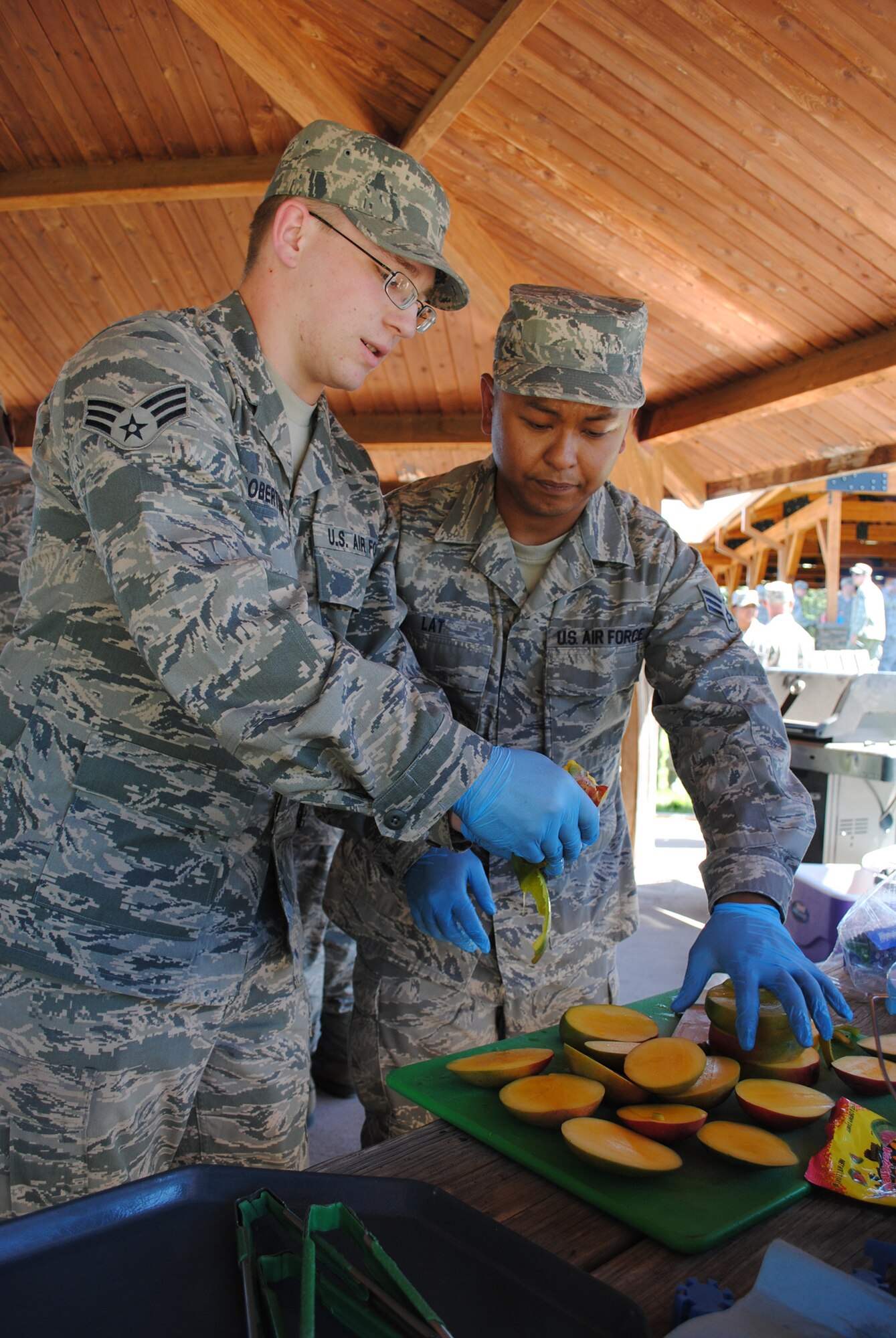 Senior Airman Brady Robertson, left, and Senior Airman Marvin Lat, both 12th Missile Squadron missile chefs, peal mangos in preparation for their dish of Korean ribs. The two incorporated Maraschino cherries into their meal by adding them to candied mangos. (U.S. Air Force photo/Airman 1st Class Katrina Heikkinen)