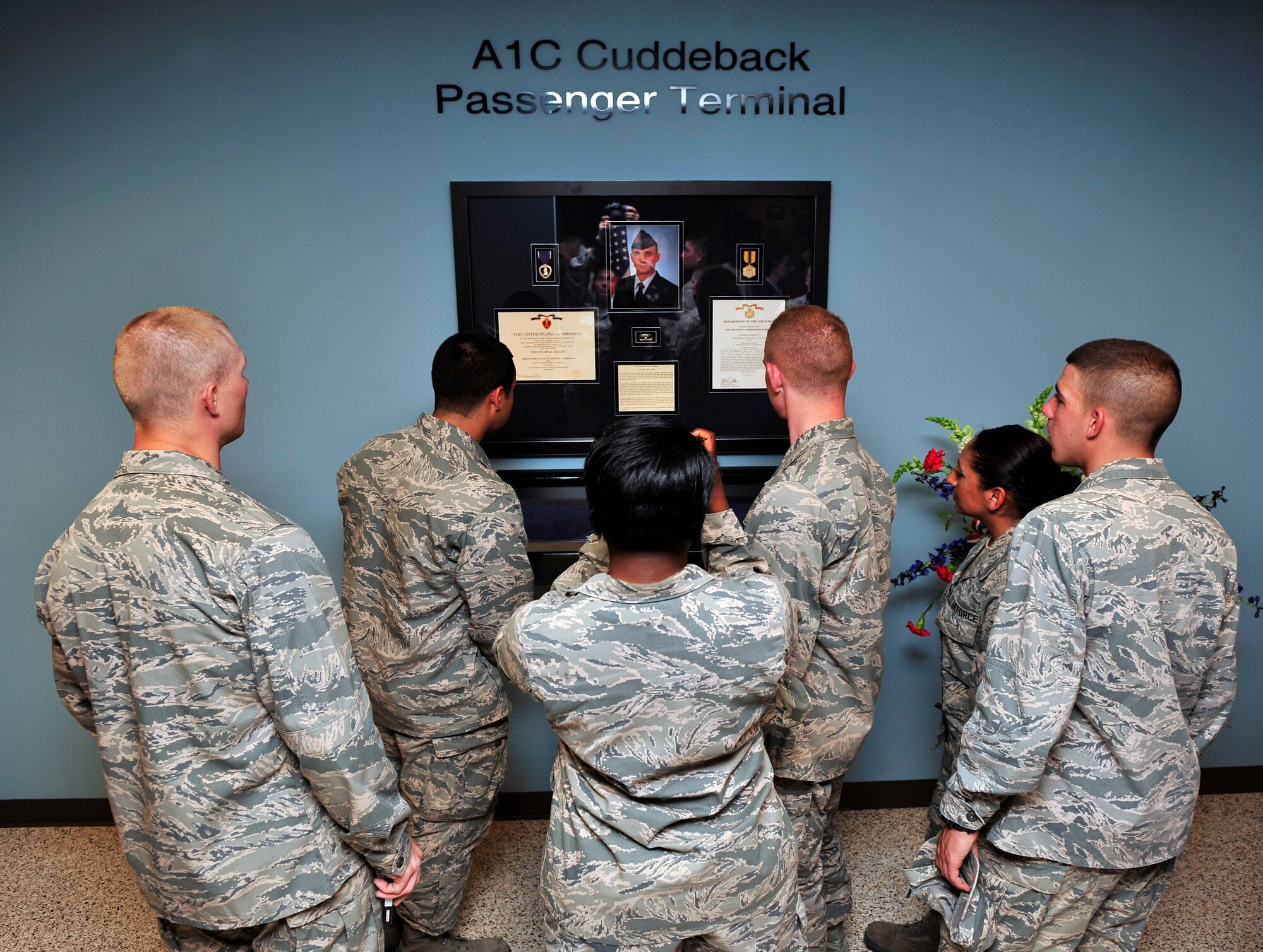 Members of Scott Air Force Base and guests admire the display of information about Airman 1st Class Zachary Ryan Cuddeback after Scott dedicated the terminal to him during a ceremony July 9, 2012. The display includes his medals, a flag and history of his service. Zachary was a vehicle operator assigned to Ramstein Air Base, Germany when he was mortally wounded March 2, 2011 by a terrorist while transporting Air Force Security Force members to the airport. (U.S. Air Force photo/ Staff Sgt. Stephenie Wade)