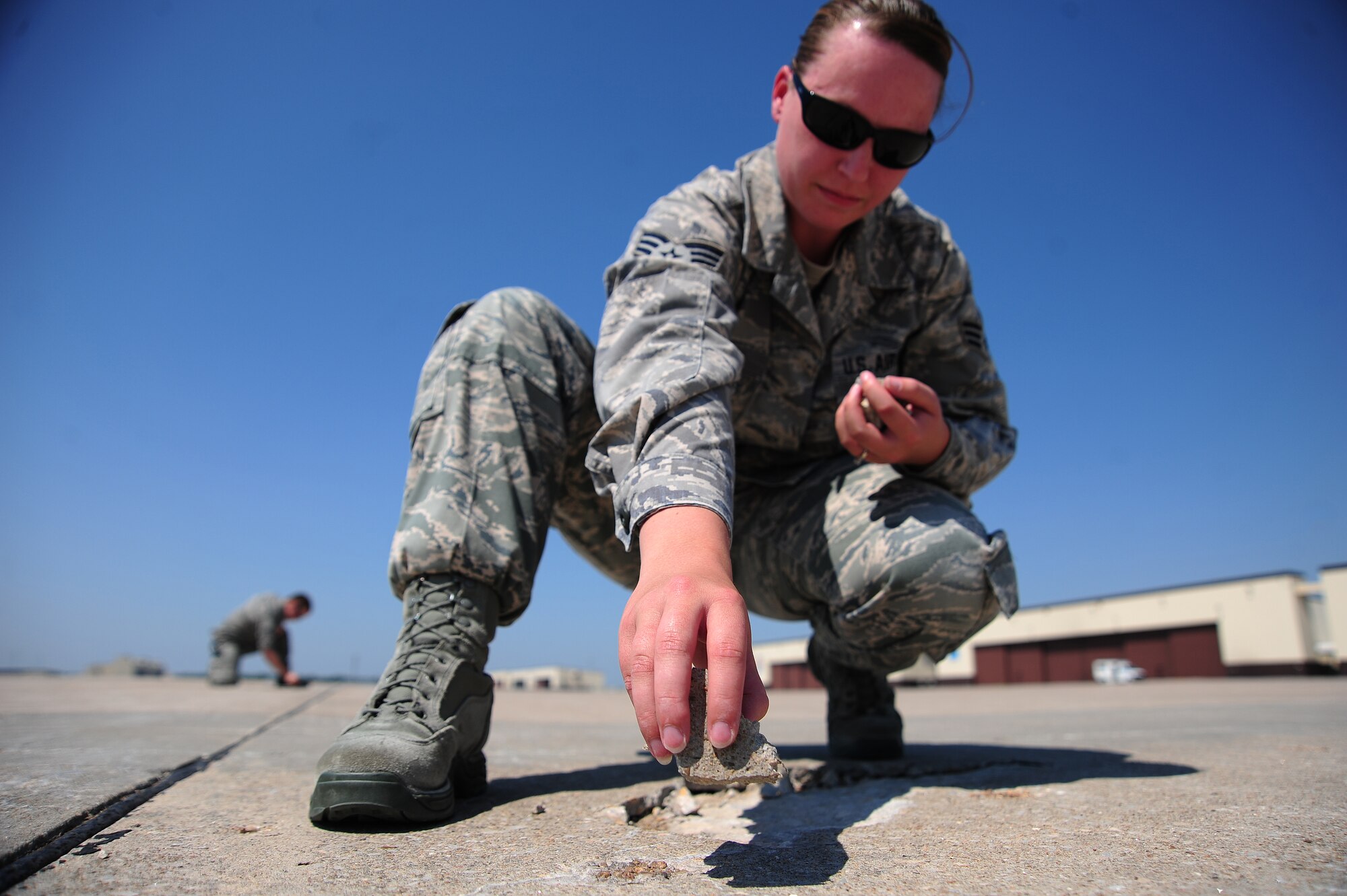 WHITEMAN AIR FORCE BASE, Mo. -- Senior Airman Alisha Thiher, 509th Operations Support Squadron airfield management journeyman, collects loose pieces of pavement from the flightline as part of an inspection June 29, for items that could cause foreign object damage.  FOD can be caused by any number of things including rocks, bags, garbage or objects dropped from aircraft. The smallest piece of FOD can destroy an entire aircraft engine. (U.S. Air Force photo/Senior Airman Nick Wilson) (Released)