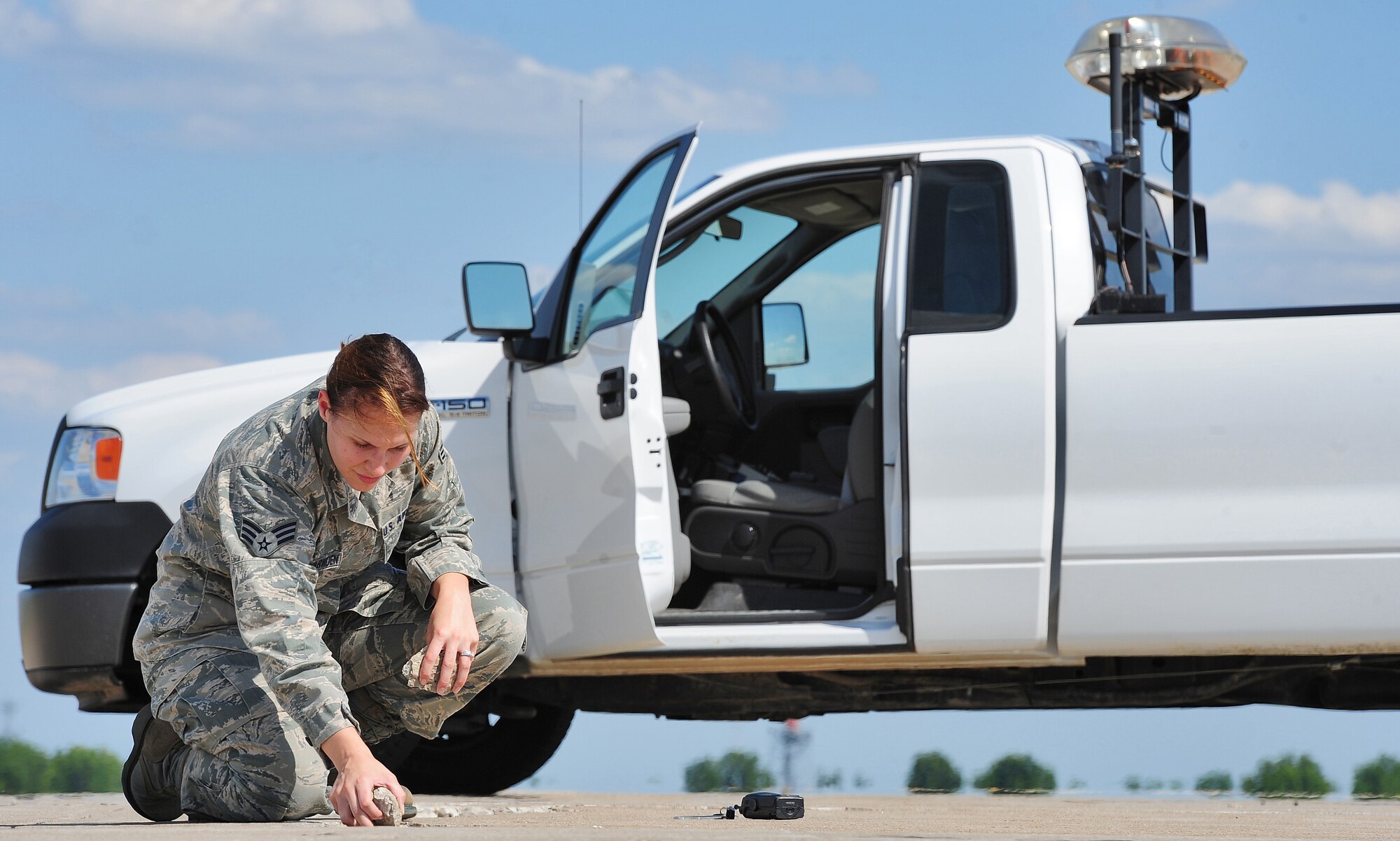 WHITEMAN AIR FORCE BASE, Mo. -- Senior Airman Alessandra Aceves-Harnden, 509th Operations Support Squadron airfield management shift lead, collects loose pieces of concrete from the flightline as part of an inspection for items that could cause foreign object damage June 7. Because weak or cracking pavement can severly damage aircraft, its maintenance is imperative for the safety of aircraft movement. (U.S. Air Force photo/Senior Airman Nick Wilson) (Released)