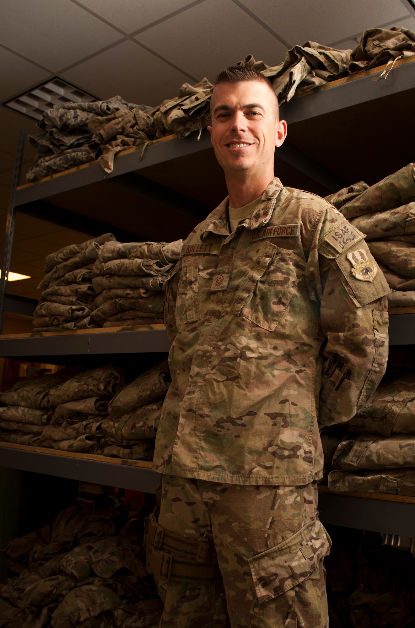 MSgt Nicholas Kollett, First Sergeant for the 455th Expeditionary Aircraft Maintenance Squadron stands in front of shelves of recycled Operation Enduring Freedom Camouflage Pattern uniforms at Bagram Airfield, Afghanistan, July 7, 2012. To date, Kollett has reissued over 1,000 OCP uniform sets, valued at over $250,000, to BAF Airmen at no cost, providing comfort from arid temperatures and facilitating a safer working environment. (U.S. Air Force photo/Capt. Raymond Geoffroy)