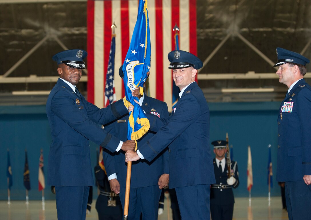 Col. Bill M. Knight, right, assumes command of the 11th Wing and Joint Base Andrews as Maj. Gen. Darren W. McDew, Air Force District of Washington commander, hands him the 11th Wing guidon during the 11th Wing Change of Command ceremony held in Hangar 3 here July 6. (Photo/Bobby Jones)