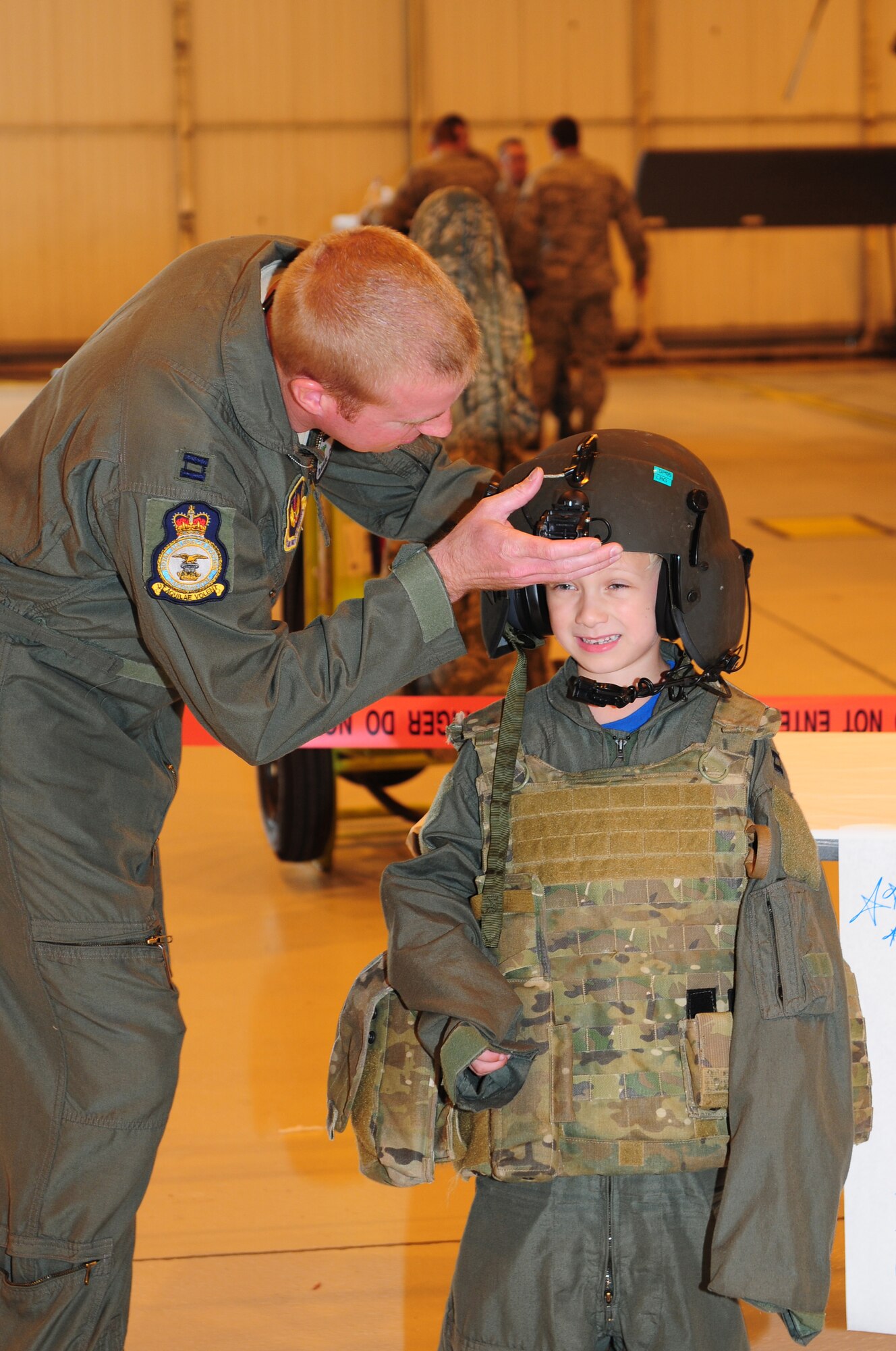 ROYAL AIR FORCE LAKENHEATH, England – Capt. Daniel Coughlin, 48th Fighter Wing flight safety, fits flight gear on Payton Kuranda during the 56th Rescue Squadron spouses’ day July 6, 2012. The 56th RQS hosted a day at the squadron featuring incentive flights for more than 50 family members as well as jumping castles and coloring activities for children. (U.S. Air Force photo by Airman 1st Class Cory D. Payne)