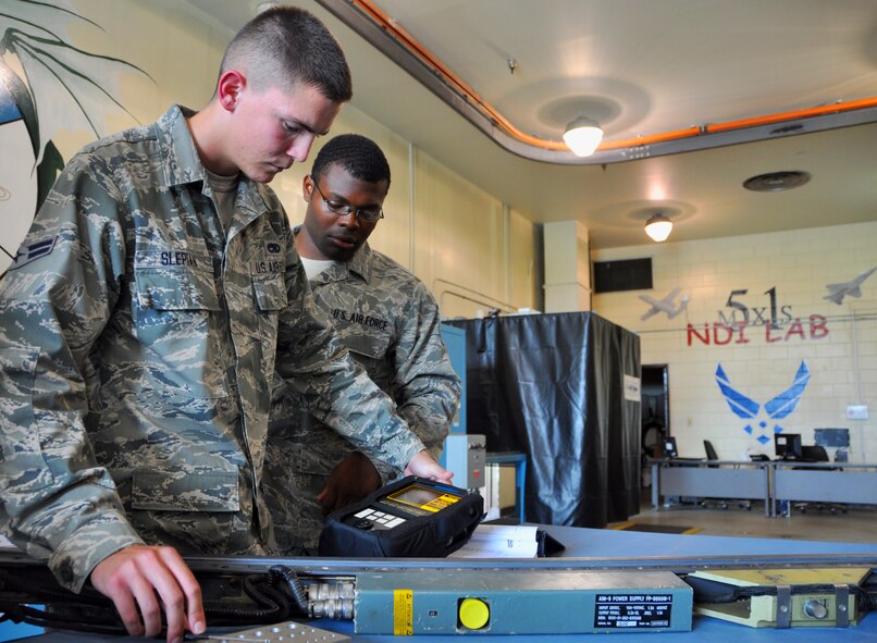 Airman 1st Class Myles Slepian looks for cracks in aircraft metals using eddy currents as Senior Airman Terrance Kelley watches July 6, 2012. The 51st Maintenance Squadron Non-destructive Inspection Flight's job is to inspect support equipment, aircraft and weapon system components for structural damage, flaws, cracks, voids, heat damage and stress fractures. Slepian is a NDI apprentice, and Kelley is a NDI journeyman. (U.S. Air Force photo/Staff Sgt. Stefanie Torres)