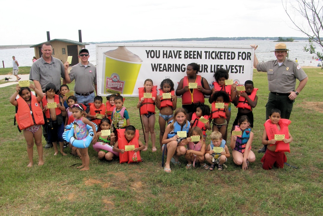DENISON, Texas — Tommy Holder (left), and Josh Wingfield, both Park Rangers with the U.S. Army Corps of Engineers Tulsa District, along with Student Conservation Association intern Matt Mueller pose with a group of children who have learned about water safety at Lake Texoma. The Tulsa District has teamed with Wendy's to "ticket" children "caught" wearing life jackets. Each ticket is good for a free Frosty.

