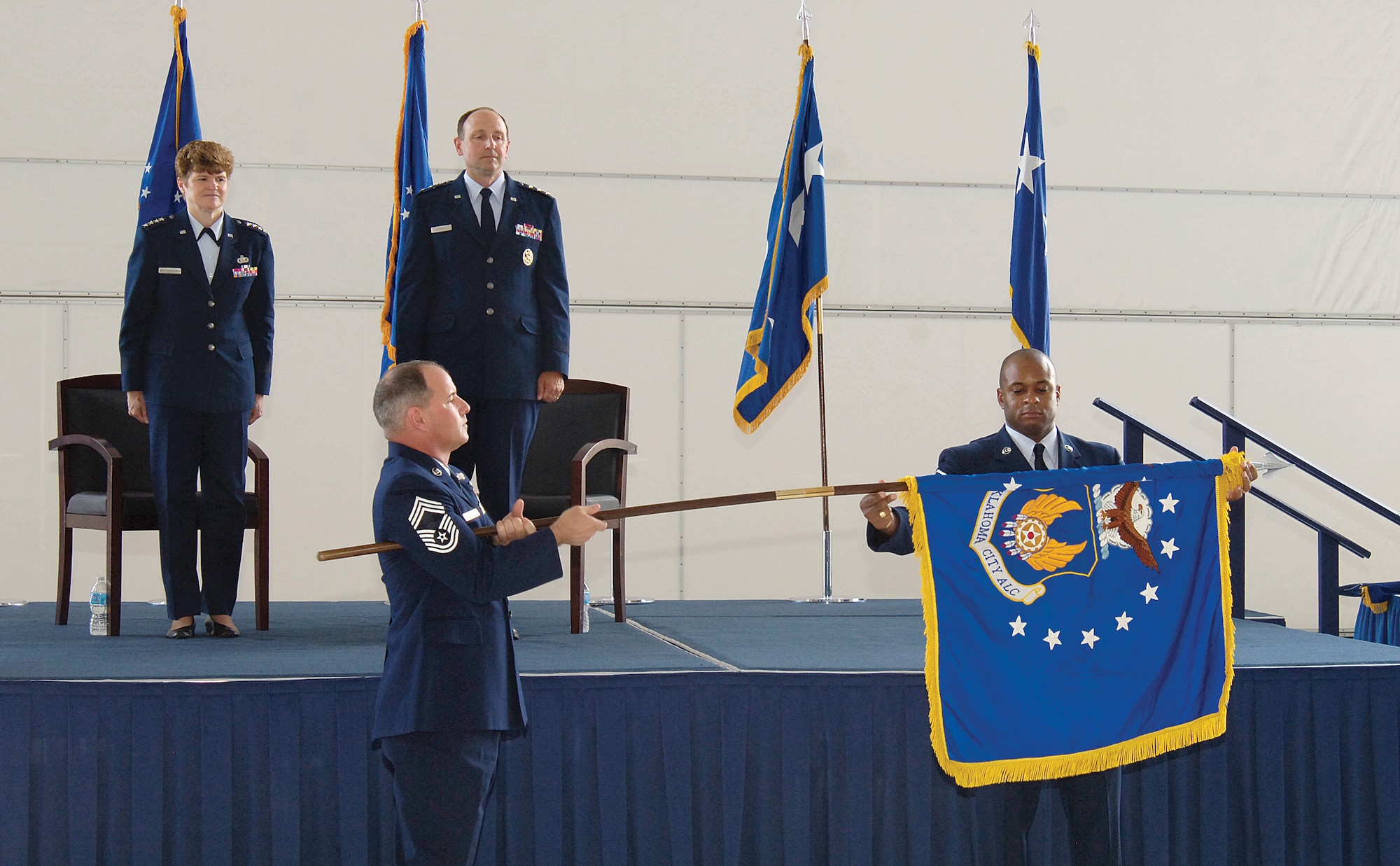 Gen. Janet Wolfenbarger, Air Force Materiel Command commander, and Lt. Gen. Bruce Litchfield, Air Force Sustainment Center commander, look on as Chief Master Sgt. Scott Magoon and Master Sgt. Albert Bryant, both from the 76th Aircraft Maintenance Group, unfurl the Oklahoma City Air Logistics Complex flag during the Air Force Sustainment Center Activation Ceremony at Tinker Air Force Base July 10. (U.S. Air Force photo/Margo Wright)