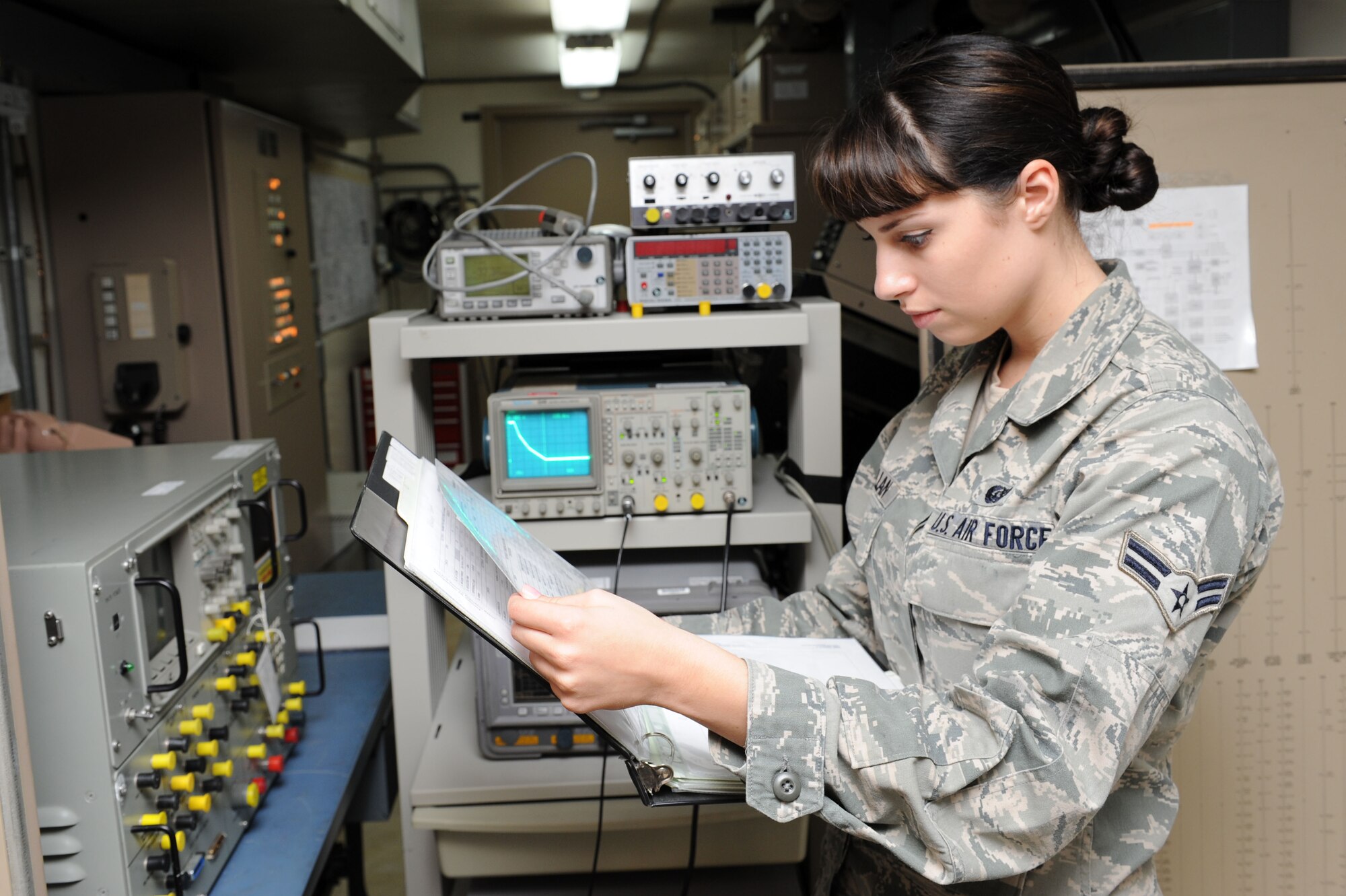 SPANGDAHLEM AIR BASE, Germany – Airman 1st Class Megan McMillan, 52nd Communications Squadron ground radar systems technician, verifies the sensitivity time control readout on an oscilloscope using a reference book at the ground radar maintenance shop here July 10. The inspection ensures air traffic controllers have a legible indicator to monitor air traffic. Ground radar systems provide data used by air traffic controllers to manage Spangdahlem air space for U.S. and NATO aircraft. (U.S. Air Force photo by Senior Airman Christopher Toon/Released)