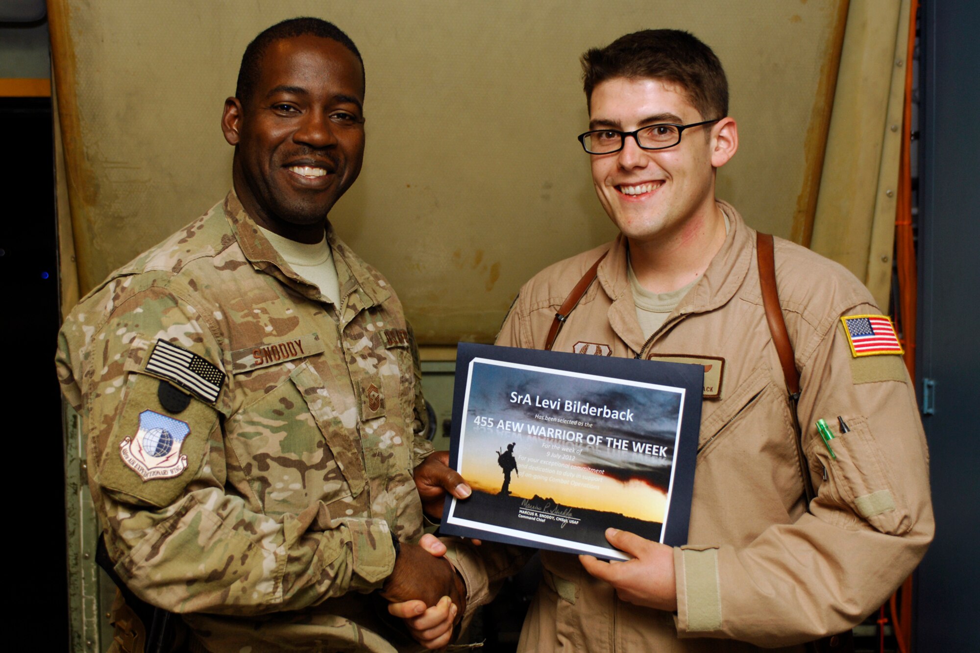 CMSgt Marcus Snoddy, 455th Air Expeditionary Wing command chief, presents the Warrior of the Week award to Senior Airman Levi Bilderback, 41st Expeditionary Electronic Combat Squadron EC-130H Compass Call analysis operator, at Bagram Airfield, Afghanistan, July 10, 2012. Bilderback operates computer assisted information warfare equipment and performs emergency procedure actions as needed on the EC-130H. He’s flown 15 combat missions and accumulated 79 hours in support of 24 International Security Assistance Force and Task Force Joint Tactical Air Support Requests. (U.S. Air Force photo/SSgt Jeff Nevison)