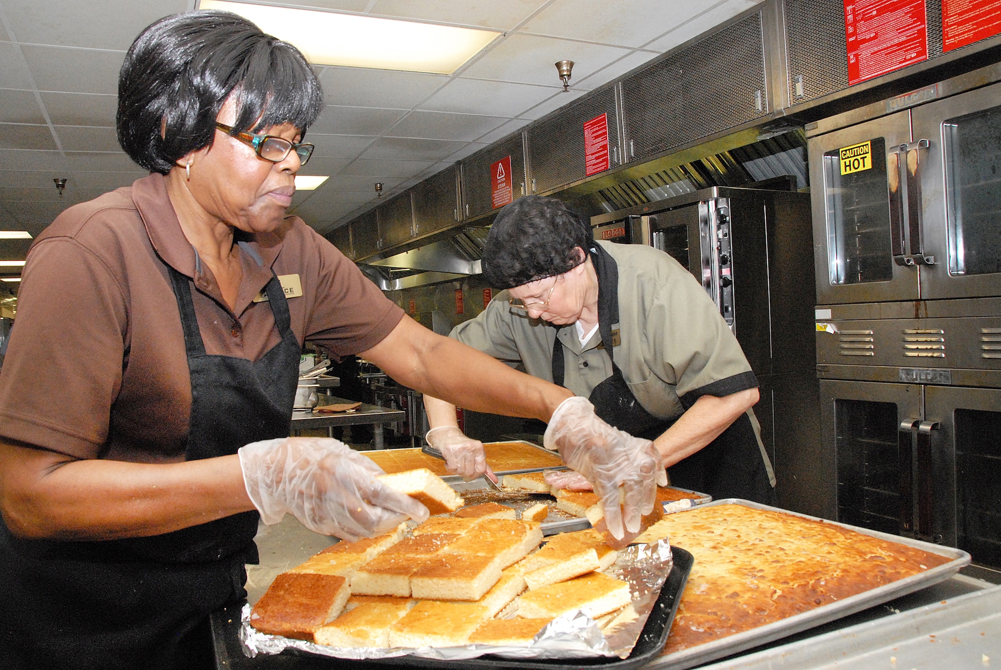 Liz Simmons and Alice Foster,food service workers, cut pans of cornbread into individual servings. (U. S. Air Force photo/Misuzu Allen)