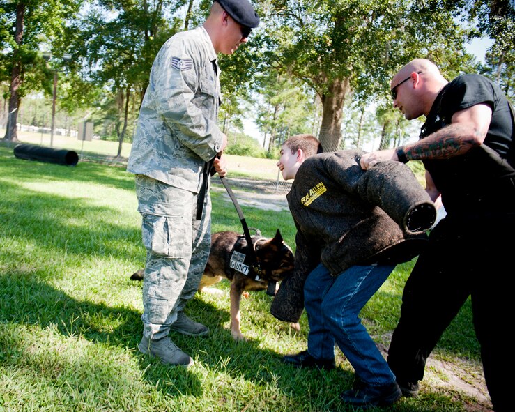 Christopher Carswell absorbs a bite from a military working dog with help from U.S. Air Force Staff Sgt. Andrew Fischer, left, and Tech. Sgt. David Smith, 23d Security Forces Squadron MWD handlers, at Moody Air Force Base, Ga., July 10, 2012. Christopher said the best part of the day with the canine unit was watching and participating in the dog bite demonstrations. (U.S. Air Force photo by Staff Sgt. Jamal D. Sutter/Released) 