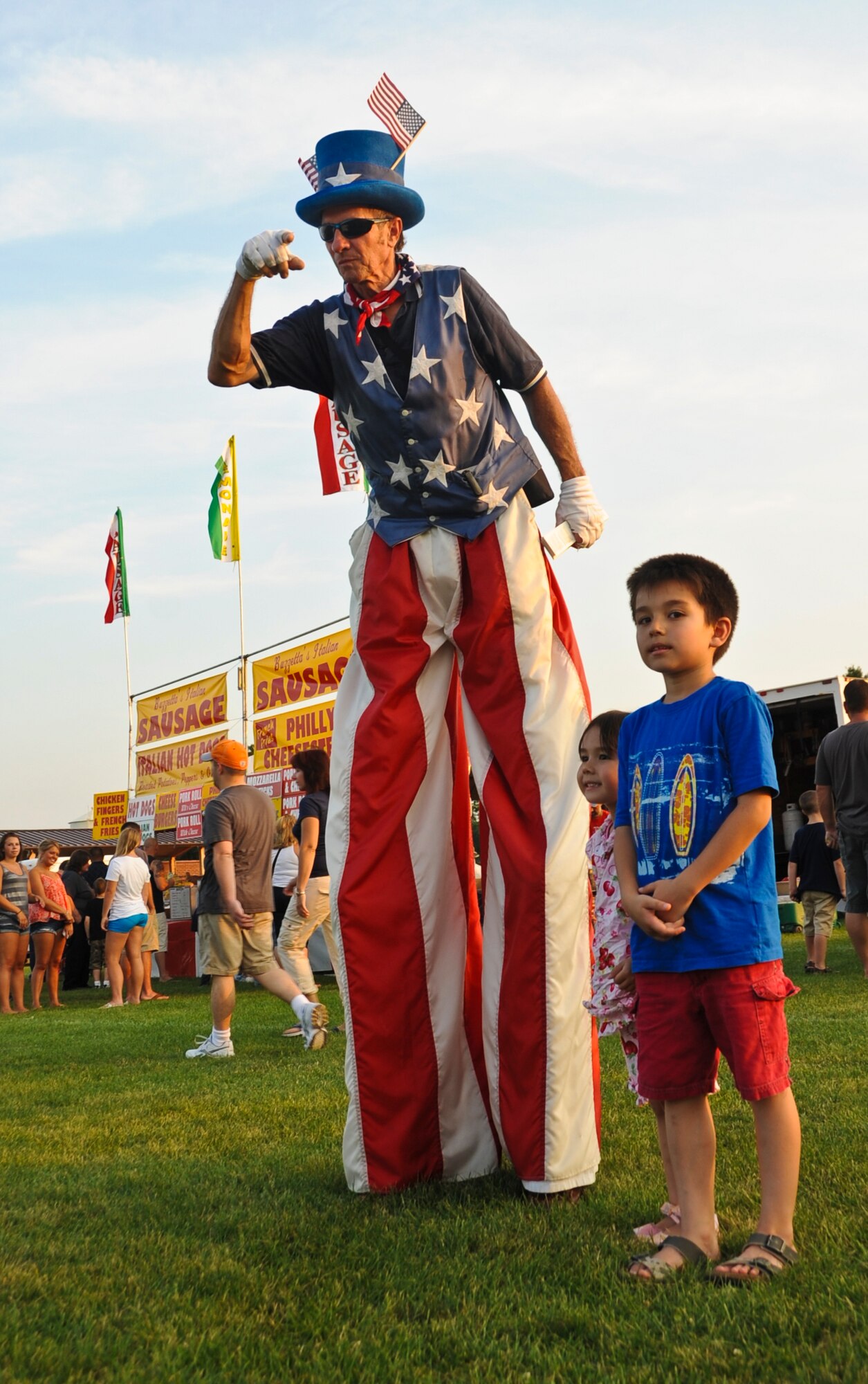 Children pose for a photo with stilt walker Ronald Maslanka during the annual Fourth of July celebration at Doughboy Field July 4 here. Thousands of people attended this year’s annual on-base celebration. (U.S. Air Force photo by Staff Sgt. David Carbajal/Released)