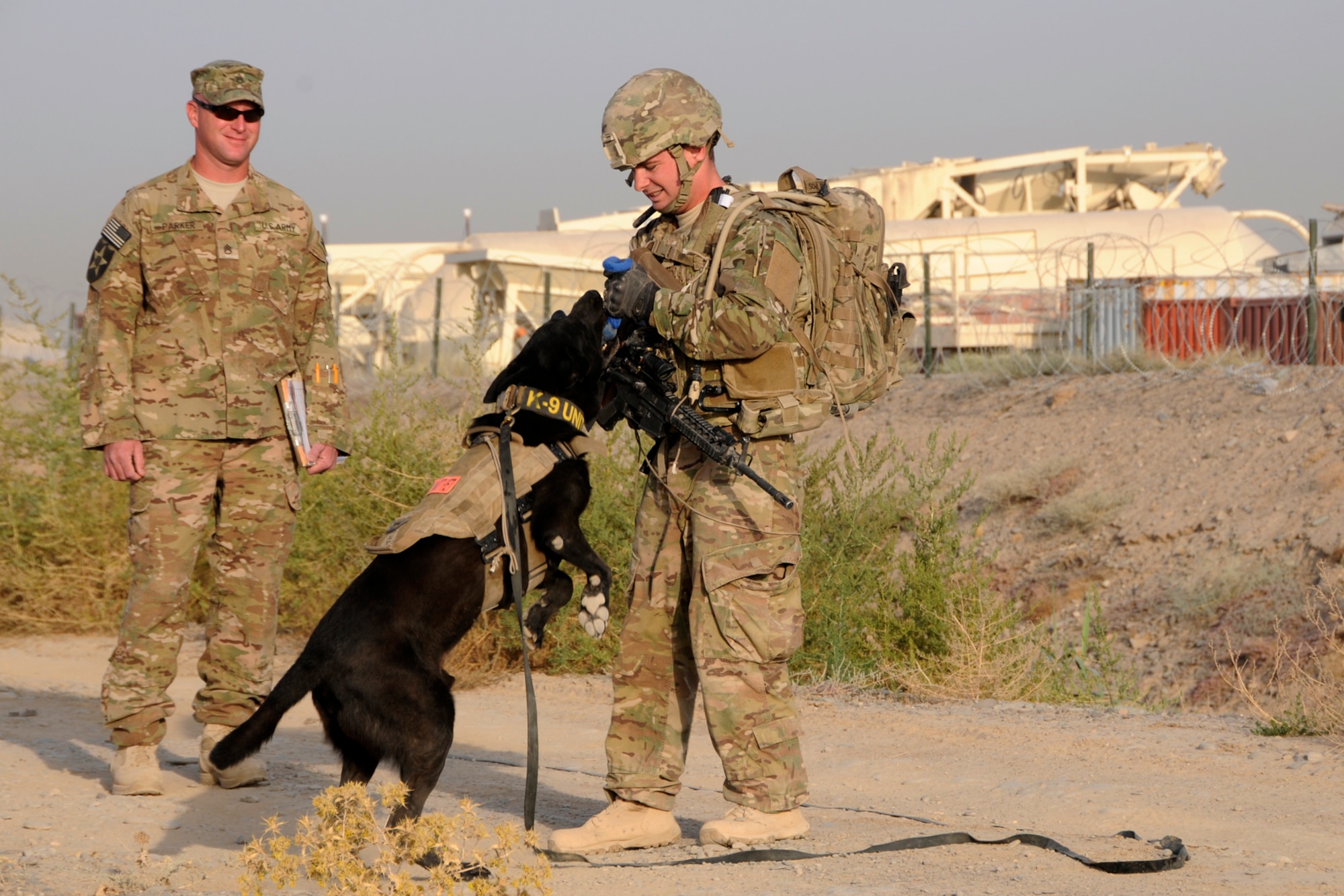 U.S. Air Force Staff Sgt. Larry Harris, a Military Working Dog handler, rewards his dog, Aaron, for finding simulated explosives buried along a road at Kandahar Airfield, Afghanistan on July 9, 2012 during a training exercise while U.S. Army Staff Sgt. Joshua Parker looks on. The handlers and their dogs rotate through Kandahar Airfield for validation prior to moving out to Forward Operating Bases around the country where they will lead combat foot patrols and sniff out IEDs and other explosives. (U.S. Air Force photo/TSgt. Stephen Hudson) 