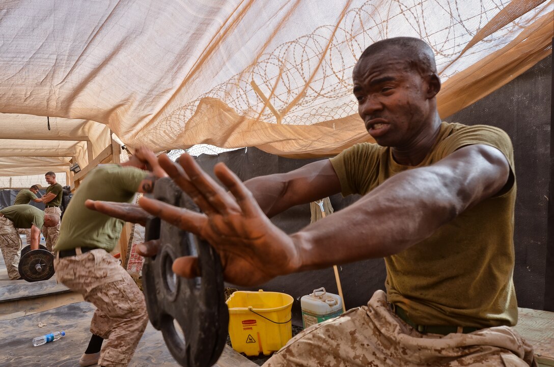 Cpl. Lud G. Romain, assistant supply warehouse chief, Headquarters and Service Company, Combat Logistics Battalion 4, 1st Marine Logistics Group (Forward), holds a weight at arm’s length during a workout here, July 14. The combat conditioning session marked the end of the seven-week course.