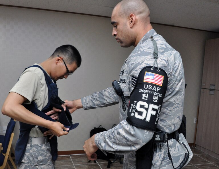 Staff Sgt. Gavin Ward, 51st Security Forces Squadron town patrolman, helps a Korean Augmentee to the U.S. Army put on bullet proof vest before going on a patrol of the Songtan Entertainment District, just outside the gates of Osan Air Base, July 12, 2012. The patrol highlights the importance of joint partnership in law enforcement and force protection between the U.S. military and the Republic of Korea. This is the first time KATUSAs have worked alongside U.S. Airmen on town patrol. (U.S. Air Force photo/Senior Airman Michael Battles)