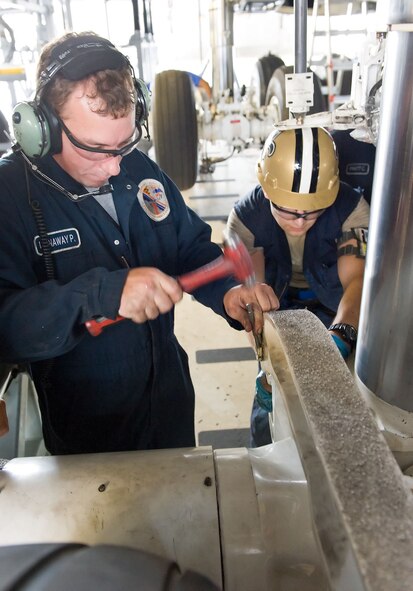 Phil Donaway, left, and Staff Sgt. Aaron Romero, aero repair technicians with the 436th Maintenance Squadron, bend a lock tab onto a nut July 16, 2012, at Dover Air Force Base, Del. The five-man team re-attached the main landing gear wheel assembly after performing required maintenance. (U.S. Air Force photo by Roland Balik)
