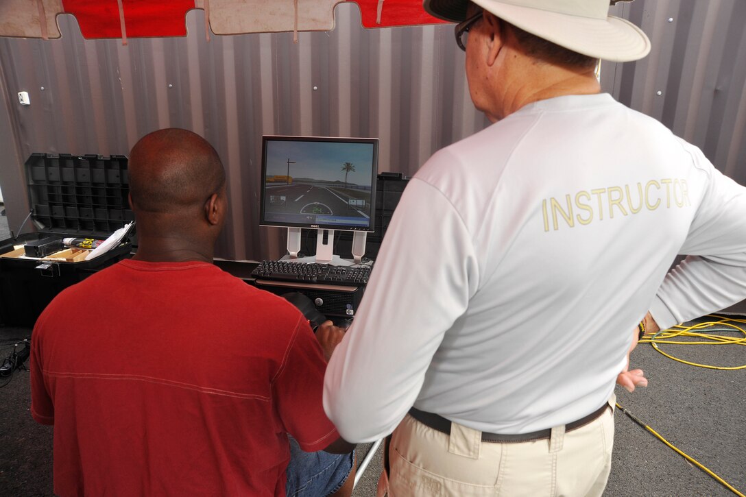 A pair of motorcycle enthusiasts take a break from the sun to test their motorcycle riding skills on a computer simulator inside a booth at Joint Base Andrews’ Motorcycle Safety Day on July 13. The computer game helped motorcycle enthusiasts and future riders experience the feel of a motorcycle ride without actually getting on a vehicle. In addition to the ride simulator booth, attendants to the Motorcycle Safety Day experienced food and game vendors, an open forum with Prince George’s County Police Department police officers and various motorcycle skill demonstrations. (U.S. Air Force photo/Senior Airman Lindsey A. Porter)
