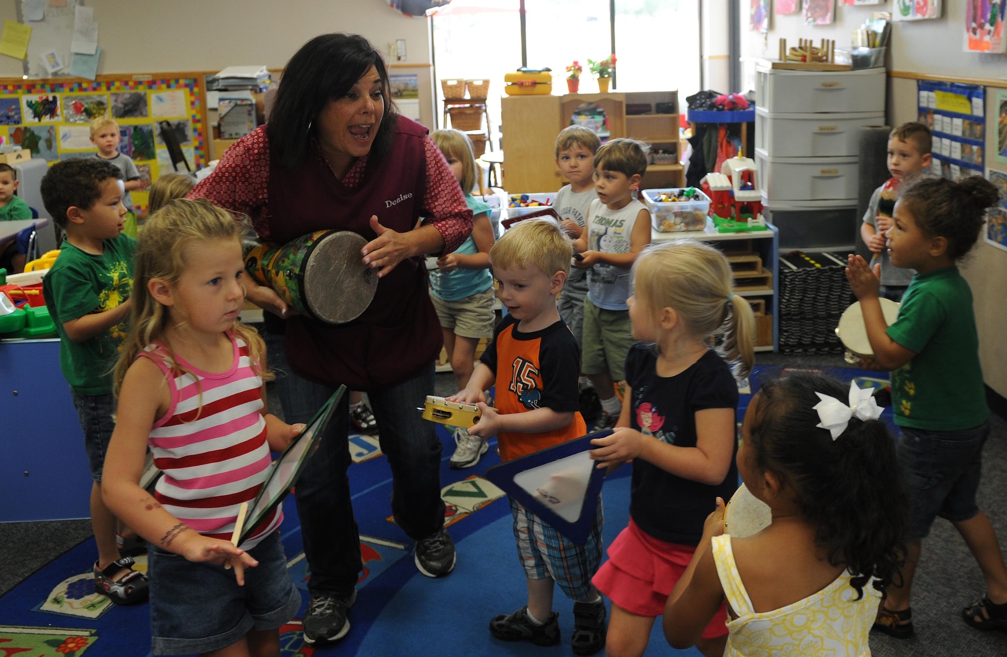 Denise Gregory, a child development program technician, sings and plays instruments with the Pre-K children during the rain dance song July 10, at Little Rock Air Force Base, Ark. The Pre-K class teaches the children to share and play together. (U.S. Air Force photo by Airman 1st Class Ellora Remington)