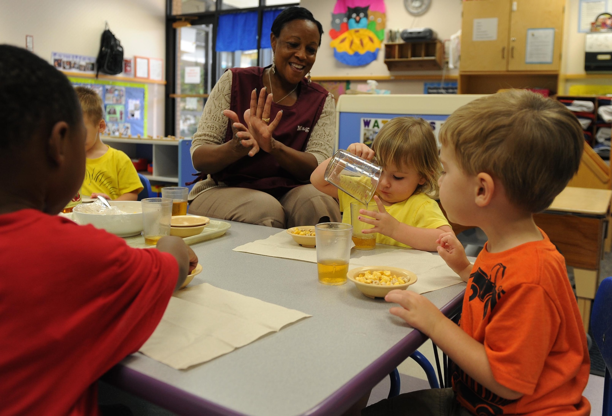 Maggie Miller, room lead teacher, helps toddlers pour juice during snack time July 10, at Little Rock Air Force Base, Ark. Teachers in the toddler room help teach the children to say ‘thank you’, ‘please’, and learn the basic table manners. (U.S. Air Force photo by Airman 1st Class Ellora Remington)