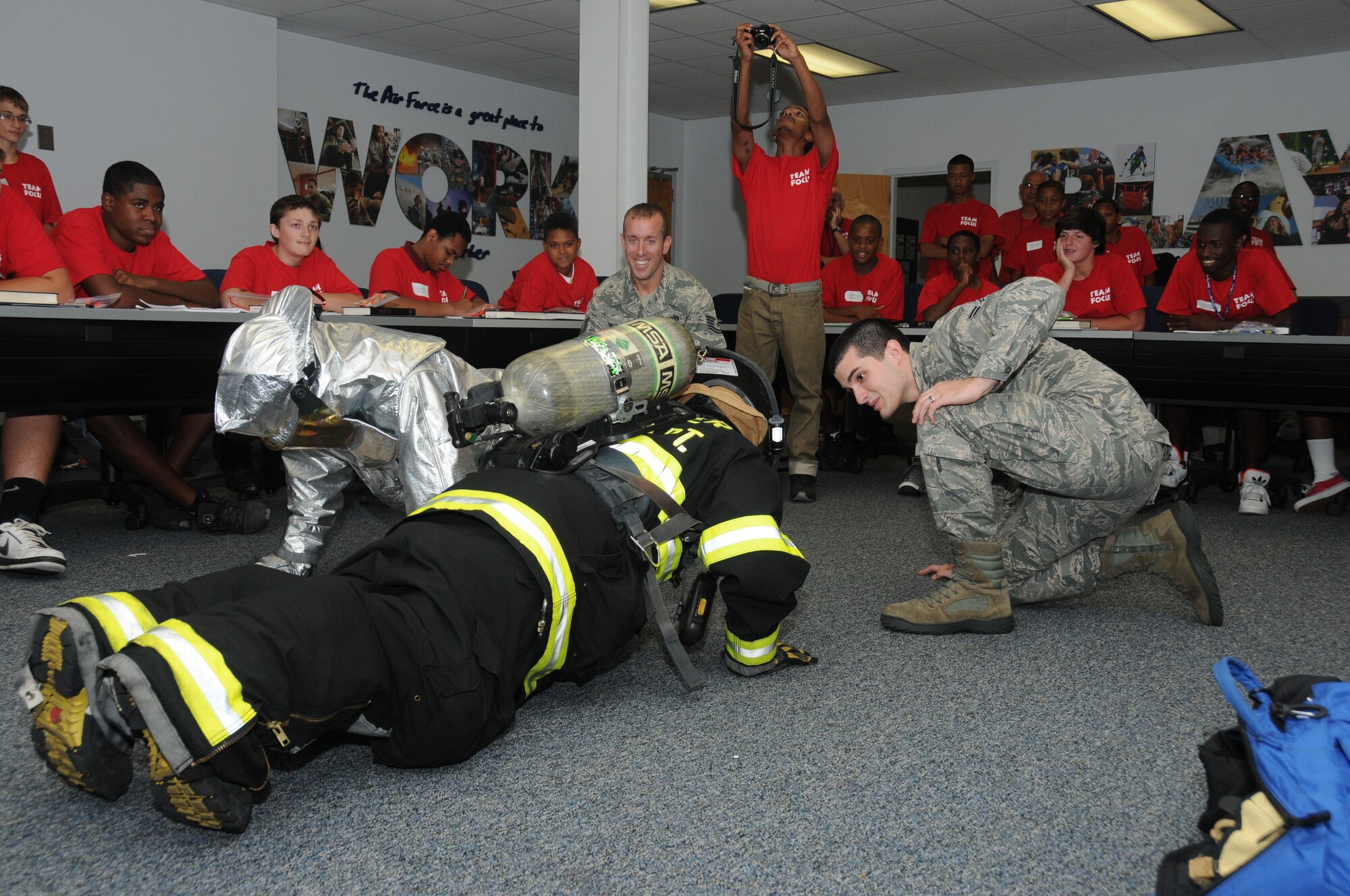 Talmadge Burton, 14, and Donald Morgan, 17, is observed by fire fighters, Tech. Sgt. Walter Shutler and Airman 1st Class Chase Dillon, attempt to do 10 push-ups while wearing fire fighter bunker gear during career night July 16, 2012, at the Sablich Center, Keesler Air Force Base, Miss.  During career night, members of various squadrons on base briefed the young men on the details of their jobs in the Air Force.  The mission of Team Focus is to provide a year-round program of support, encouragement and values that foster the development of life skills in young men ages 10-18 without a father figure in their lives, bridging the fatherless gap and supporting the family structure.  (U.S. Air Force photo by Kemberly Groue)