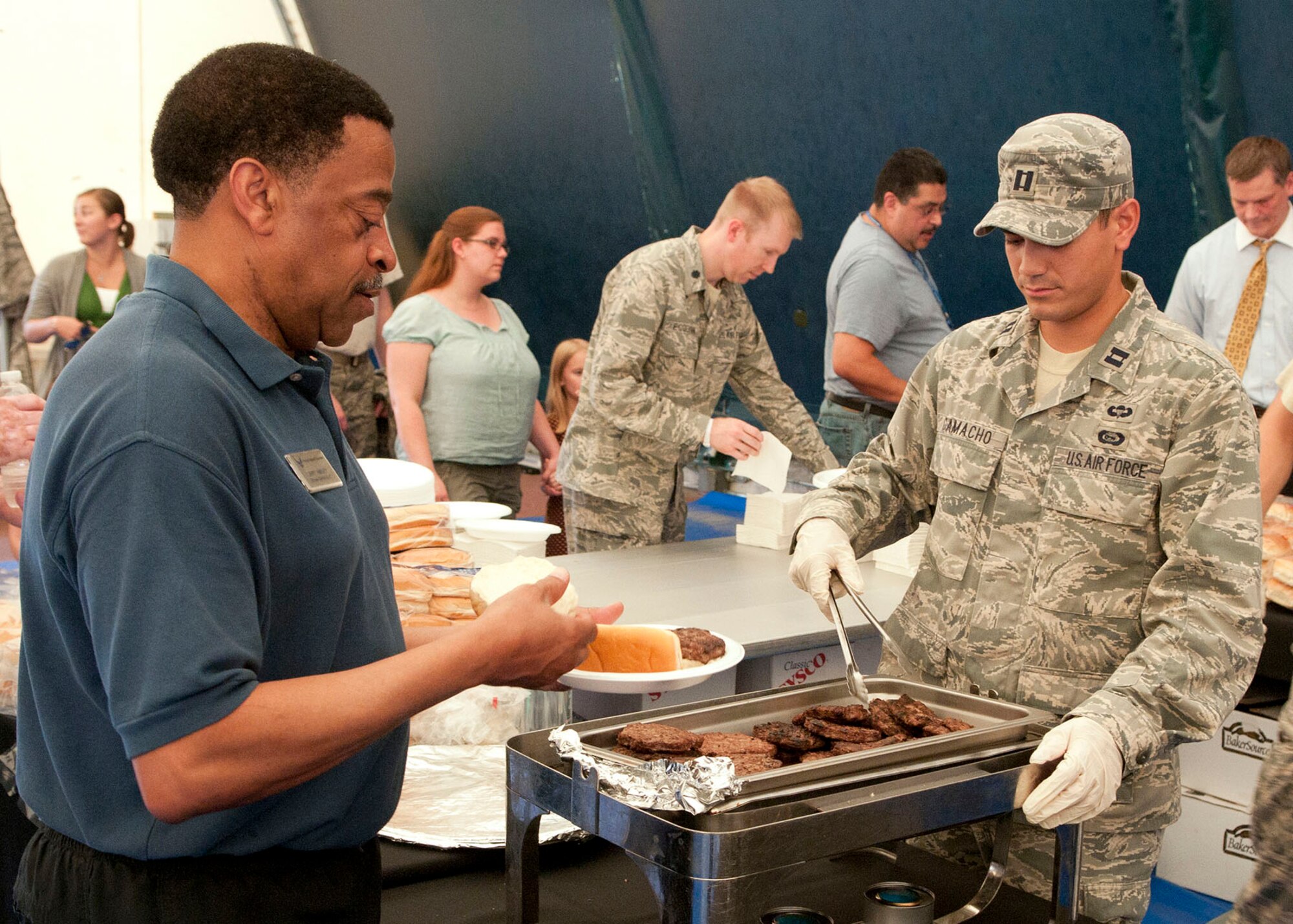 HANSCOM AIR FORCE BASE, Mass. – Capt. Sean Camacho, a deputy program manager, serves a hamburger to Larry Harvey, 66th Force Support Squadron, in the Tennis Bubble July 13. Base personnel were invited to an installation picnic to recognize the contributions made by the Hanscom community before the Electronic Systems Center transitioned to the Air Force Life Cycle Management Center. (U.S. Air Force photo by Mark Wyatt)