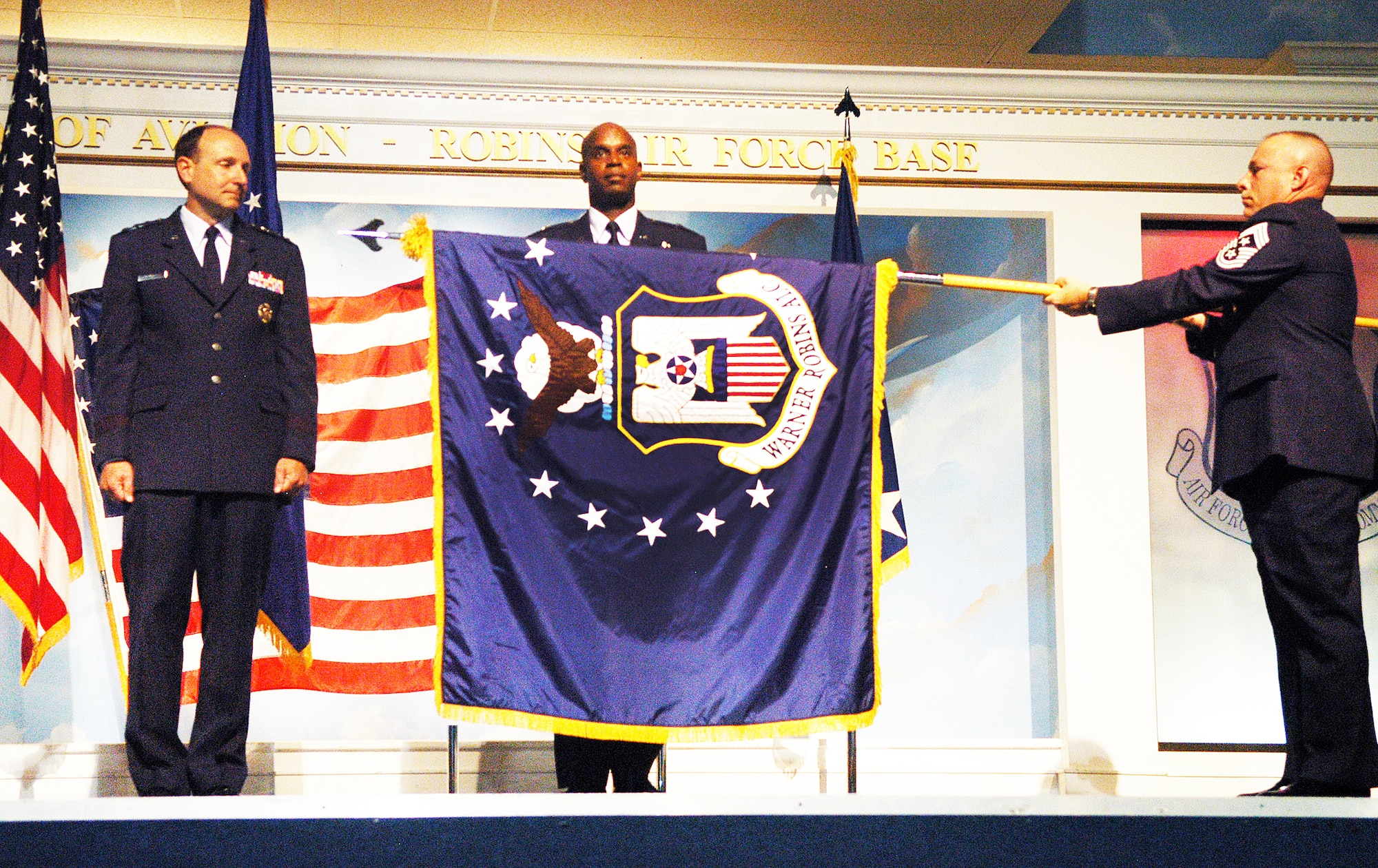 L-R, Bruce A. Litchfield, commander of the Air Force Sustainment Center and Brig. Gen. Cedric D. George, Warner Robins Air Logistic Complex commander, watch as Command Chief MSgt. Patrick Bowen unfurls the Air Logistics Complex flag.  (U. S. Air Force photo/Sue Sapp)