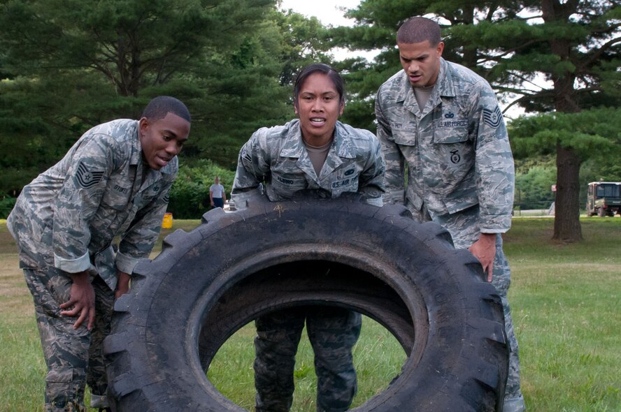 HANSCOM AIR FORCE BASE, Mass. – Airman 1st Class Charnelle S. Albino receives encouragement from Tech. Sgt. Julius H. Stokes (left) and Tech. Sgt. Scott Roy (right) as she picks up a tire during Warrior Day July 11. This group from the Security Forces Squadron placed first in the competitive team portion of Warrior Day. (U.S. Air Force photo by Rick Berry)