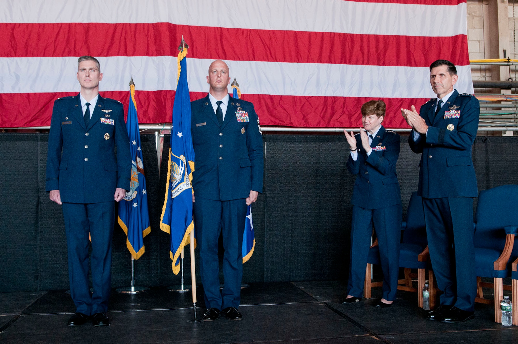 HANSCOM AIR FORCE BASE, Mass. - Gen. Janet C. Wolfenbarger, Air Force Materiel Command commander, and Lt. Gen. C.D. Moore II, Air Force Life Cycle Management Center commander, applaud while Col. Mark S. Spillman, Electronic Systems Center commander, and Chief Master Sgt. Baird Stiefel, Hanscom senior enlisted adviser, stand at attention after the citation for the Air Force Organizational Excellence Award is read. The award was presented to ESC during a transition ceremony in the Aero Club Hangar July 16 when ESC became a part of AFLCMC. (U.S. Air Force photo by Mark Wyatt)