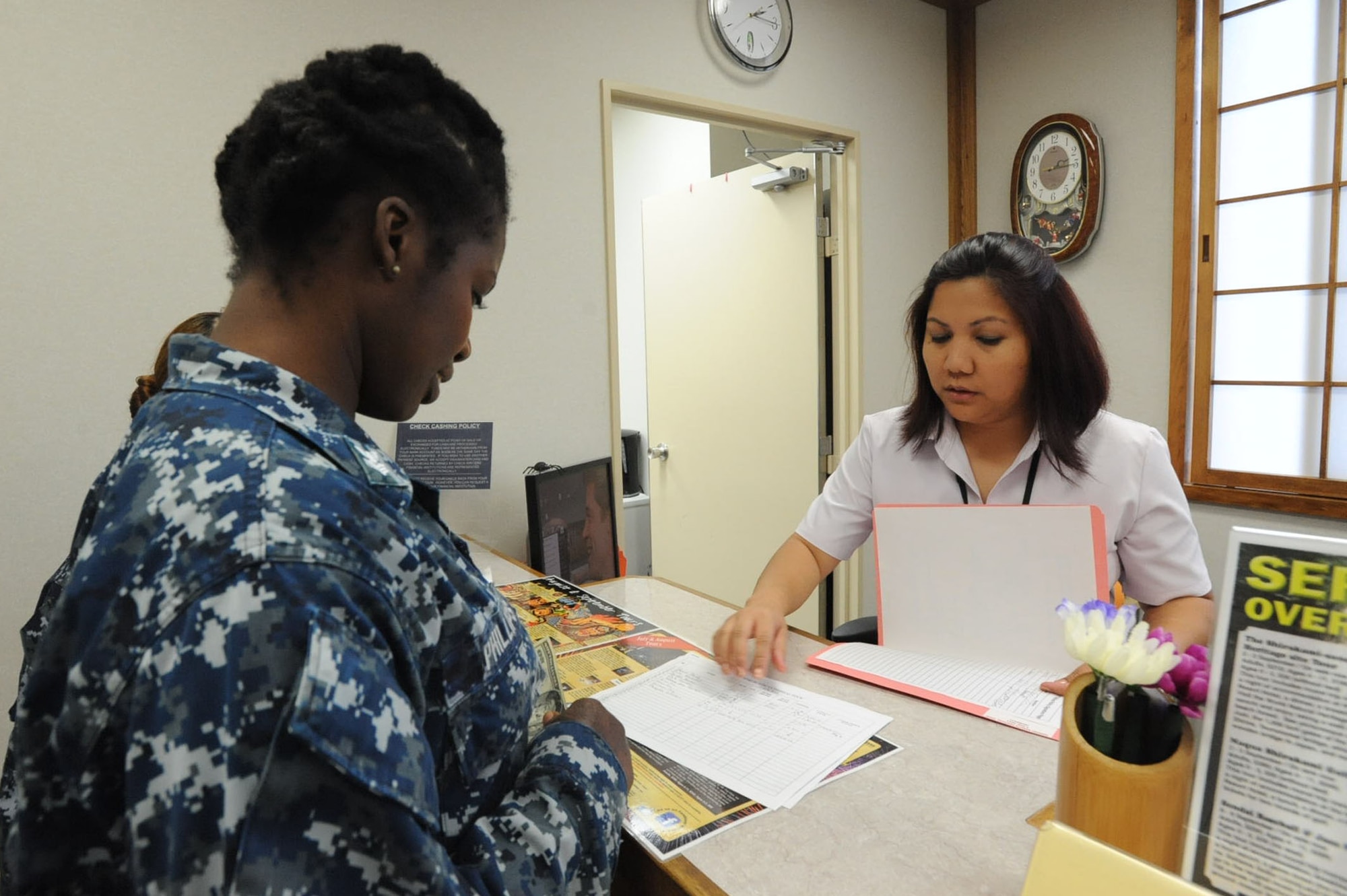 Sharon Williams, right, Misawa Air Base Information, Tickets and Travel transportation clerk, assists a sailor at Misawa Air Base, Japan, July 18, 2012. As the transportation clerk, Williams is in charge of preparing tour materials for the bus drivers and tour guides and schedules hotel reservations for tourists. Williams also educates curious travelers of the best tourist attractions, and helps make the travel experience smooth for military members wanting to explore Japan. The ITT office is open Monday to Friday from 9 a.m. to 6 p.m. On Saturdays, the shop is open from 10 a.m. to 2 p.m. (U.S. Air Force photo by Airman 1st Class Kenna Jackson/Released)