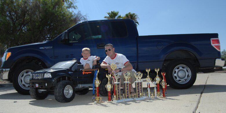 U.S. Air Force Staff Sgt. Steve Ogden, 923rd Aircraft Maintenance Squadron, and his son Greyson, age 5, pose for a picture with their respective sound system competition trucks and the myriad trophies they’ve won at Heritage Park on Davis-Monthan Air Force Base, Ariz., July 17, 2012. (U.S. Air Force photo by Airman 1st Class Michael Washburn/Released)
