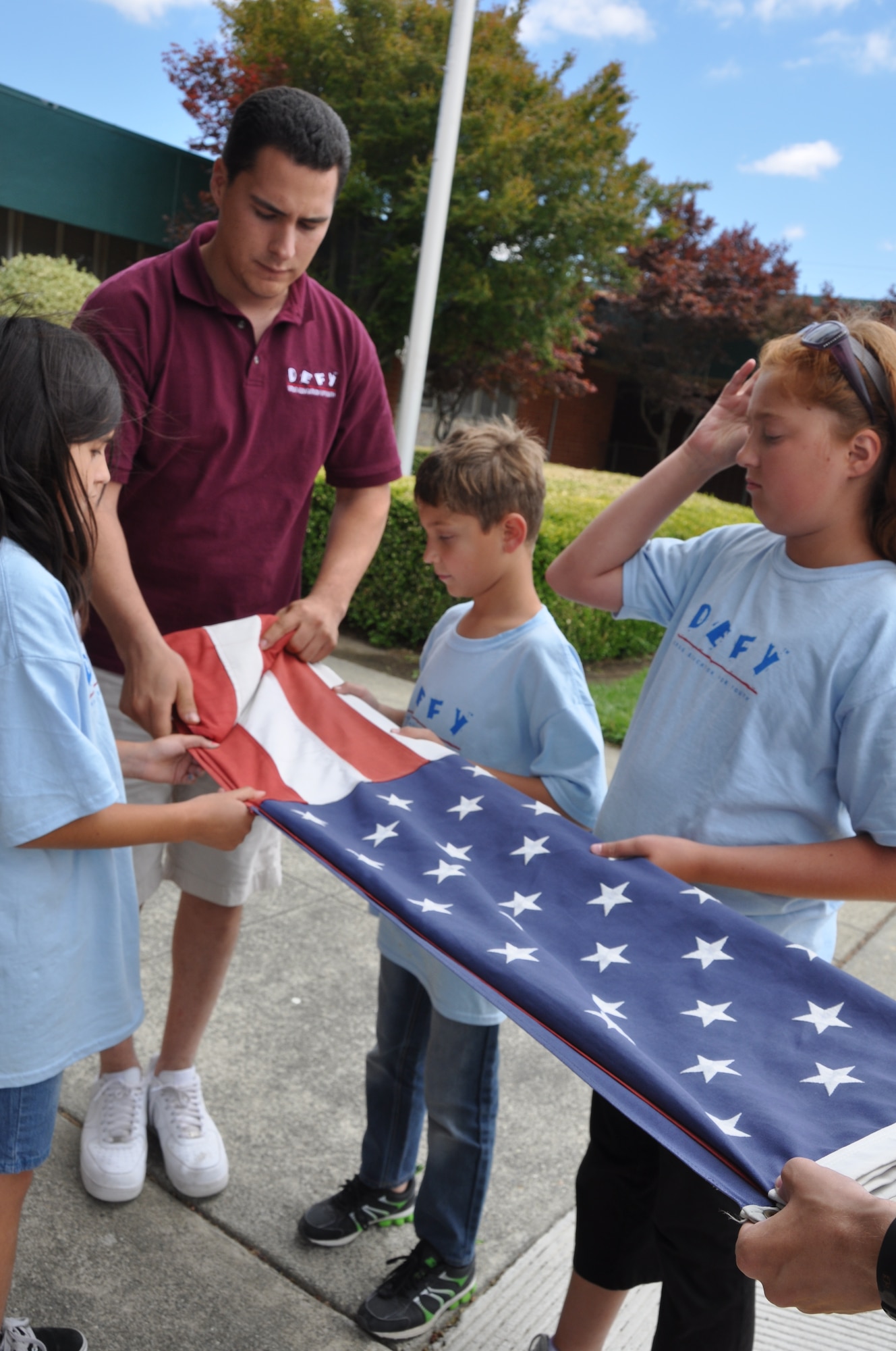 A Drug Education for Youth counselor helps a group of kids learn how to properly fold the flag July 17. (U.S. Air Force photo/2nd Lt. Jessica Clark) 