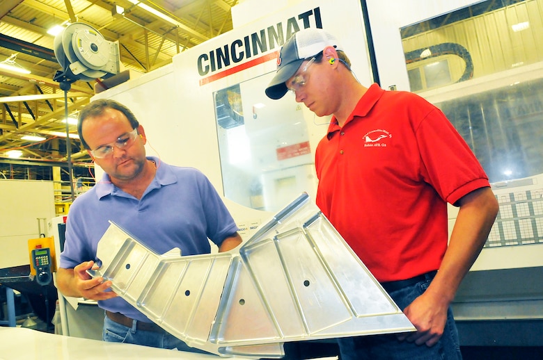 Kyle Keene and Kirk Kitchens show one of the old process C-5 end fittings and discuss the changes in the process for the new ones. (U. S. Air Force photo/Sue Sapp)