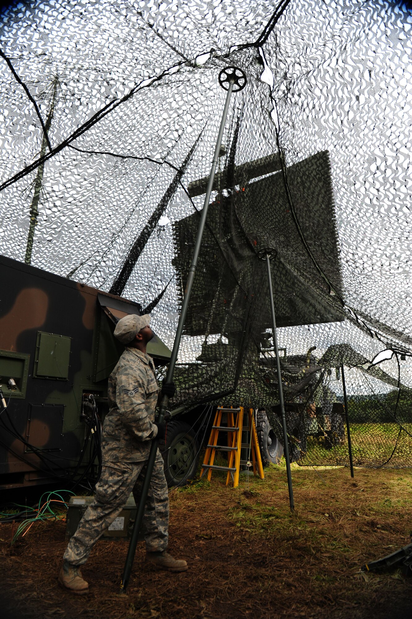 GEROLSTEIN, Germany – Senior Airman Joshua Harvey, 606th Air Control Squadron ground radar maintenance technician, hoists a camouflage cover over a radar shelter for Eifel Strike 2012 here July 16.  Eifel Strike is an annual field training exercise during which Airmen build a controlled radar site as well as a control and reporting center to work and live out of for a week. Exercises like this are designed to give Spangdahlem Airmen the practice, skills and experience they need to deploy efficiently and effectively within a moment’s notice in support of contingency operations around the world. (U.S. Air Force photo by Airman 1st Class Gustavo Castillo/Released)