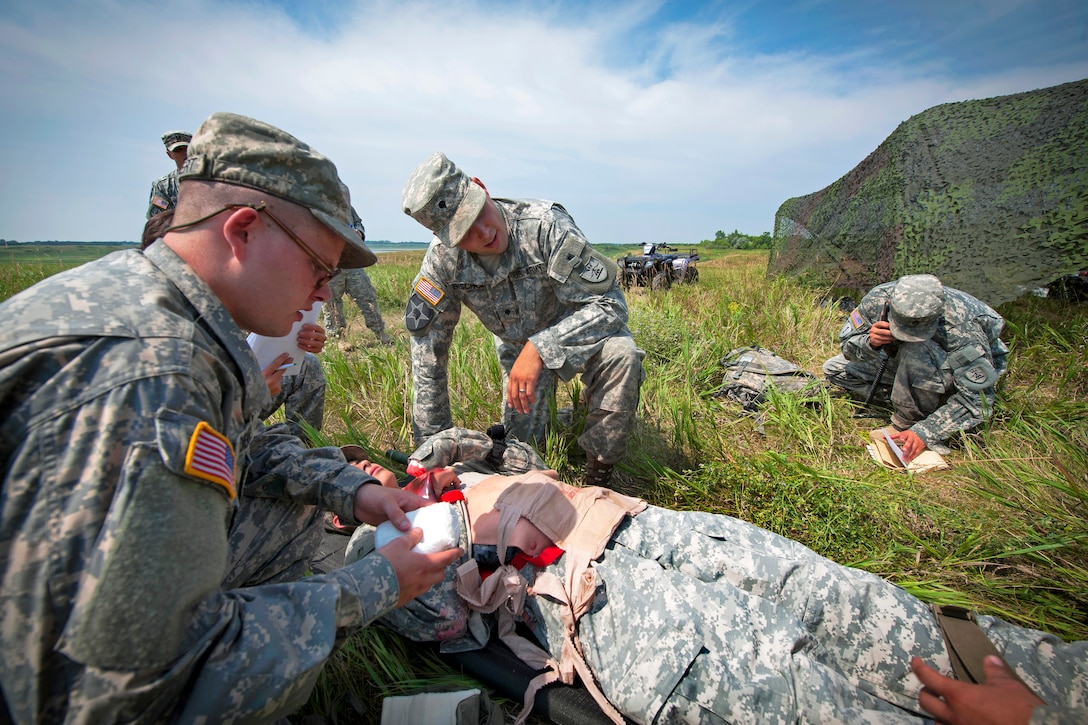 Army Spc. Jeffrey Diemert, left, and Spc. Levi Bischof, center, examine the wounds of a mock casualty at a medical station during the unit's first ever Sapper Stakes competition, while Staff Sgt David Rohrich, right, calls in for support at Pipestem Lake, outside Jamestown, N.D., July 14, 2012. Diemert, Rohrich and Bischof are assigned to the 817th Sapper Company, North Dakota Army National Guard.