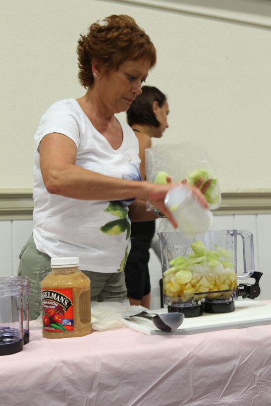 A military spouse pours cucumbers and ice into a blender while demonstrating how to create delicious and healthy smoothies at the “It’s All About You,” mid-deployment workshop at the Russell Marine and Family Center aboard the base July 7.Every participant walked away with various freebies including a wide variety of smoothie recipes.