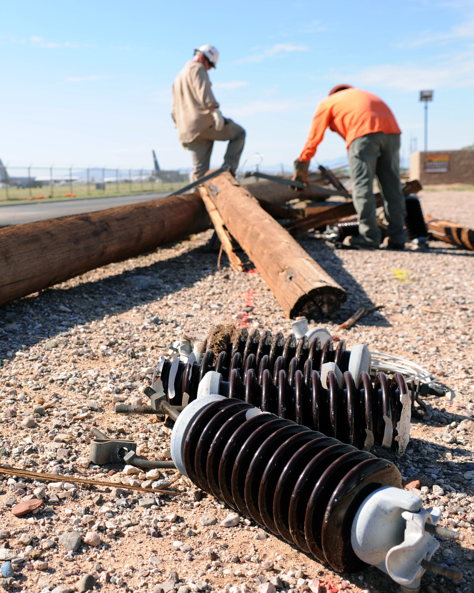 High voltage insulators from broken electric poles lie on the ground as electrical technicians from Tucson Electric Power remove parts from the broken poles on Davis-Monthan Air Force Base, Ariz., July 18, 2012. The broken lines were removed from the base two to three days after the monsoon. (U.S. Air Force photo by Airman 1st Class Christine Griffiths/Released) 