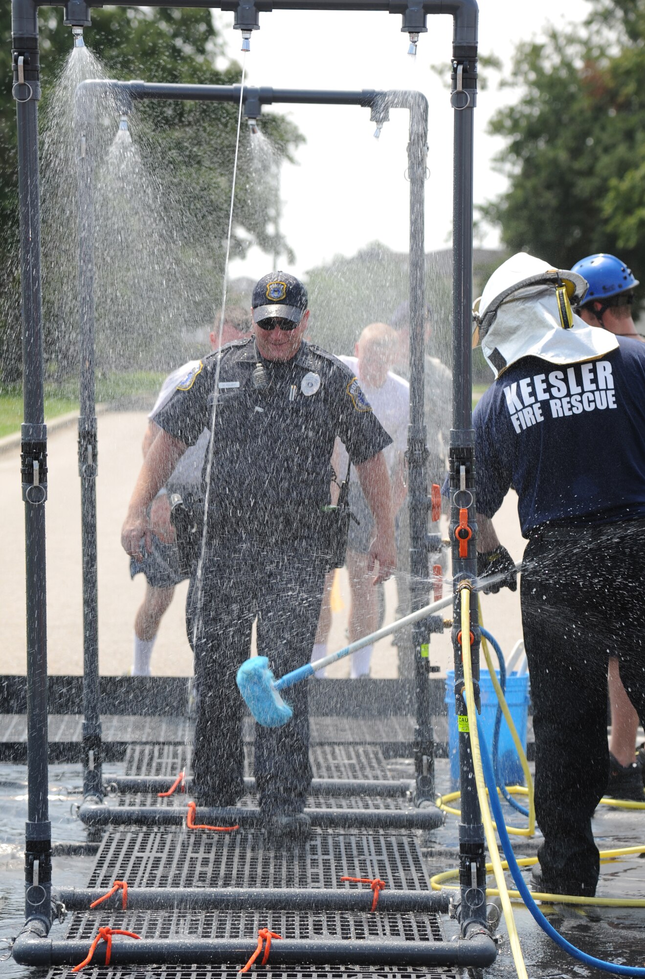 Officer Jeremy Ellzey, 81st Security Forces Squadron, is decontaminated by members of the Keesler Fire Department during an exercise July 18, 2012, at Keesler Air Force Base, Miss. Keesler held the three-day exercise to test the response of base personnel. In the exercise scenario, a disgruntled base employee sprayed harmful chemicals on Airmen in the Triangle training area injuring several people. Witnesses contacted 911 and within minutes, members of the 81st Security Forces Squadron apprehended the individual and first responders began decontamination and treatment of the victims. (U.S. Air Force photo by Kemberly Groue)