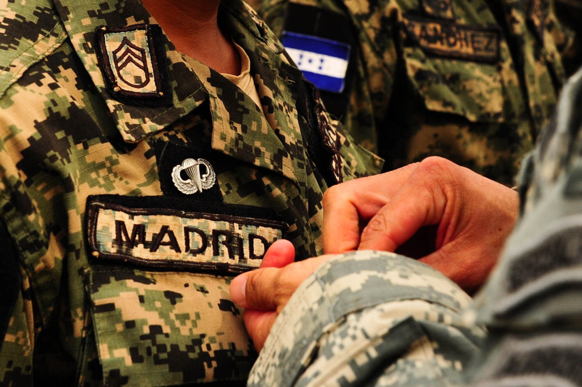 SOTO CANO AB, Honduras – A U.S. Army jumpmaster presents a Honduran paratrooper U.S. army jump wings during a wing exchange ceremony following a combined airborne exercise at Joint Task Force-Bravo.The exercise was designed to sharpen the paratroopers’ airborne proficiency and strengthen the partnership between the two militaries. (U.S. Air Force photo by 1st Lt. Christopher Diaz)