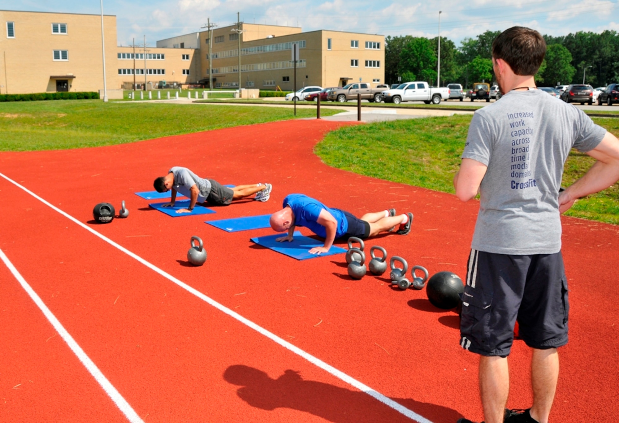 From left, Capt. Brandon Herndon and 1st Lt. Wes Meredith, under the supervision of Kevin Duncan, AEDC Fitness Center assistant, go through a full-body exercise called a “burpee” as part of their Crossfit program workout recently at the running track on base. (Photo by Jacqueline Cowan)