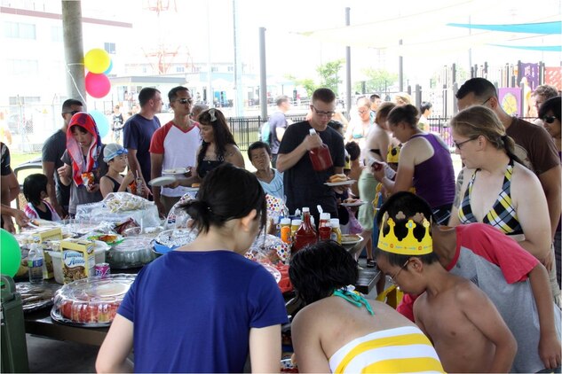 Community-relations event volunteers along with children from the Yahata Gakuen children’s home begin gathering near the food at the pool party hosted by Marine Wing Support Squadron 171 at the WaterWorks pool here July 21, 2012.::r::::n::The Yahata Gakuen children’s home is sponsored by MWSS-171.