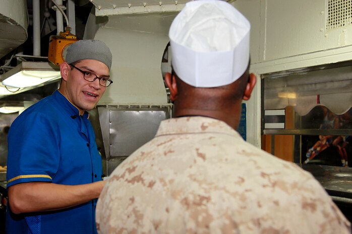 Petty Officer 3rd Class Julio J. Lopez (left,) culinary specialist, USS Peleliu, discusses food service preparation techniques with Lance Cpl. James T. Payne, food service specialist, Headquarters and Service Company, Battalion Landing Team 3/5, 15th Marine Expeditionary Unit, in the ship’s galley, July 22. Lopez, 24, is from Denver and Payne, 22, is from Memphis, Tenn. The two prepare lunch and dinner for the Marines and sailors of the 15th Marine Expeditionary Unit and Peleliu Amphibious Ready Group.